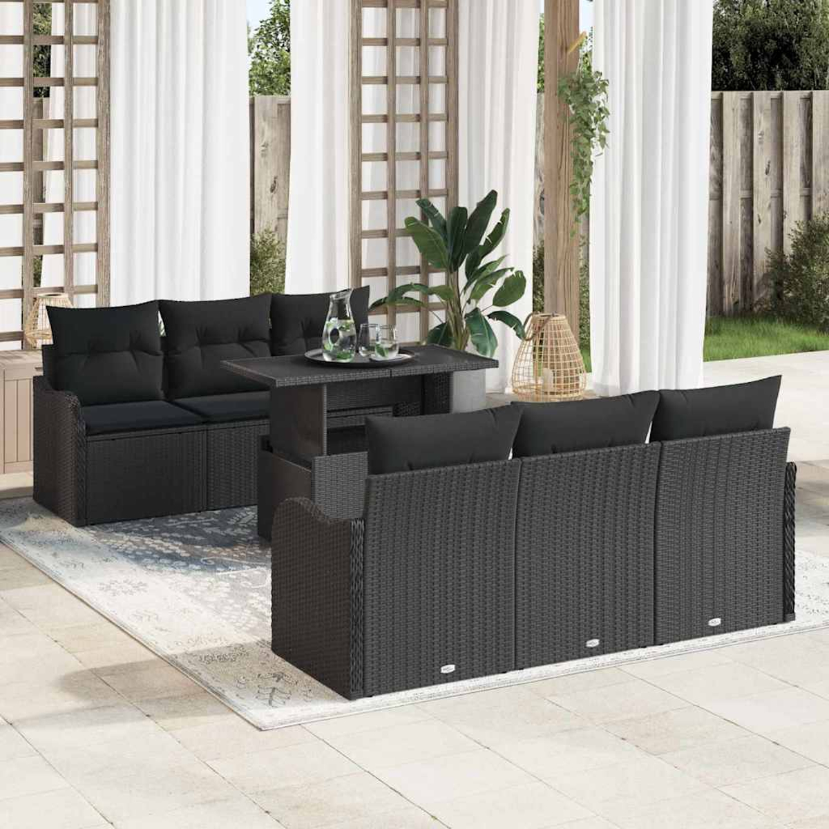 Garten-Terrassenset mit dunklen Korbmöbeln, schwarzen Kissen und einem Tisch. Weiße Vorhänge und ein Holzspalier im Hintergrund.