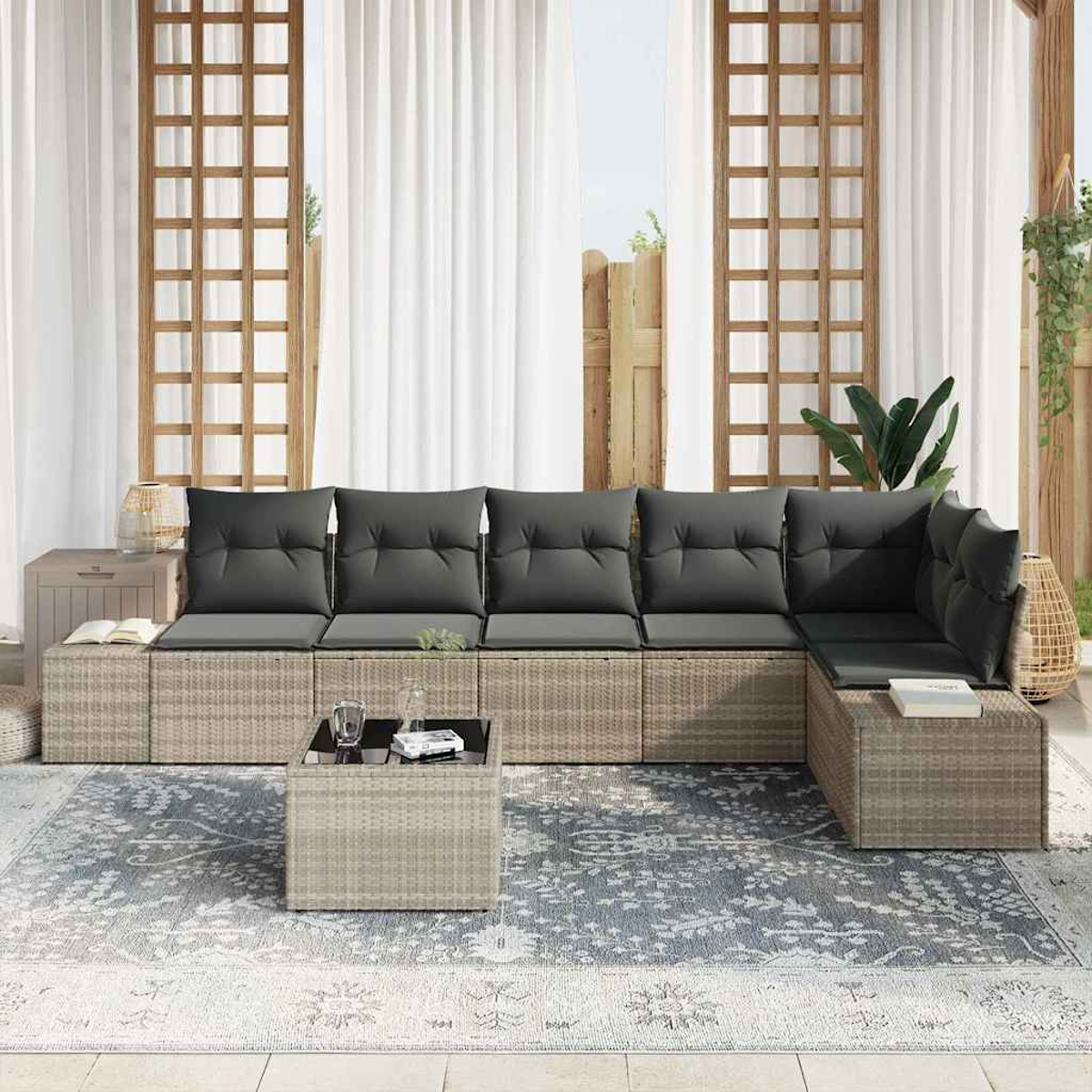 Ein Outdoor-Ecksofa mit grauen Kissen. Davor ein Couchtisch und ein gemusterter Teppich. Weiße Vorhänge und Holzgitter im Hintergrund.