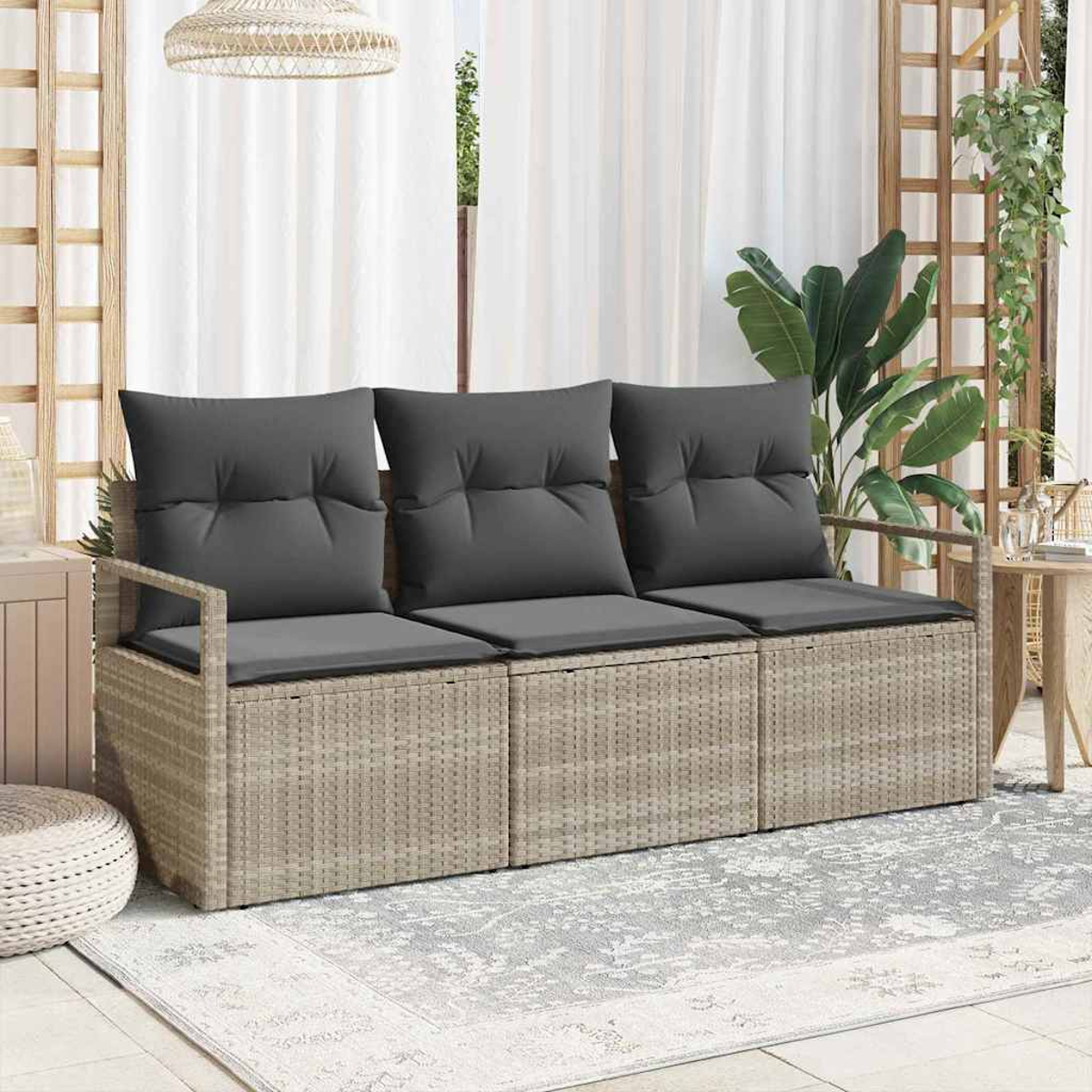 Rattansofa mit grauen Kissen. Dahinter weiße Vorhänge und eine Pflanze. Die Szene spielt sich auf einem gemusterten Teppich ab.