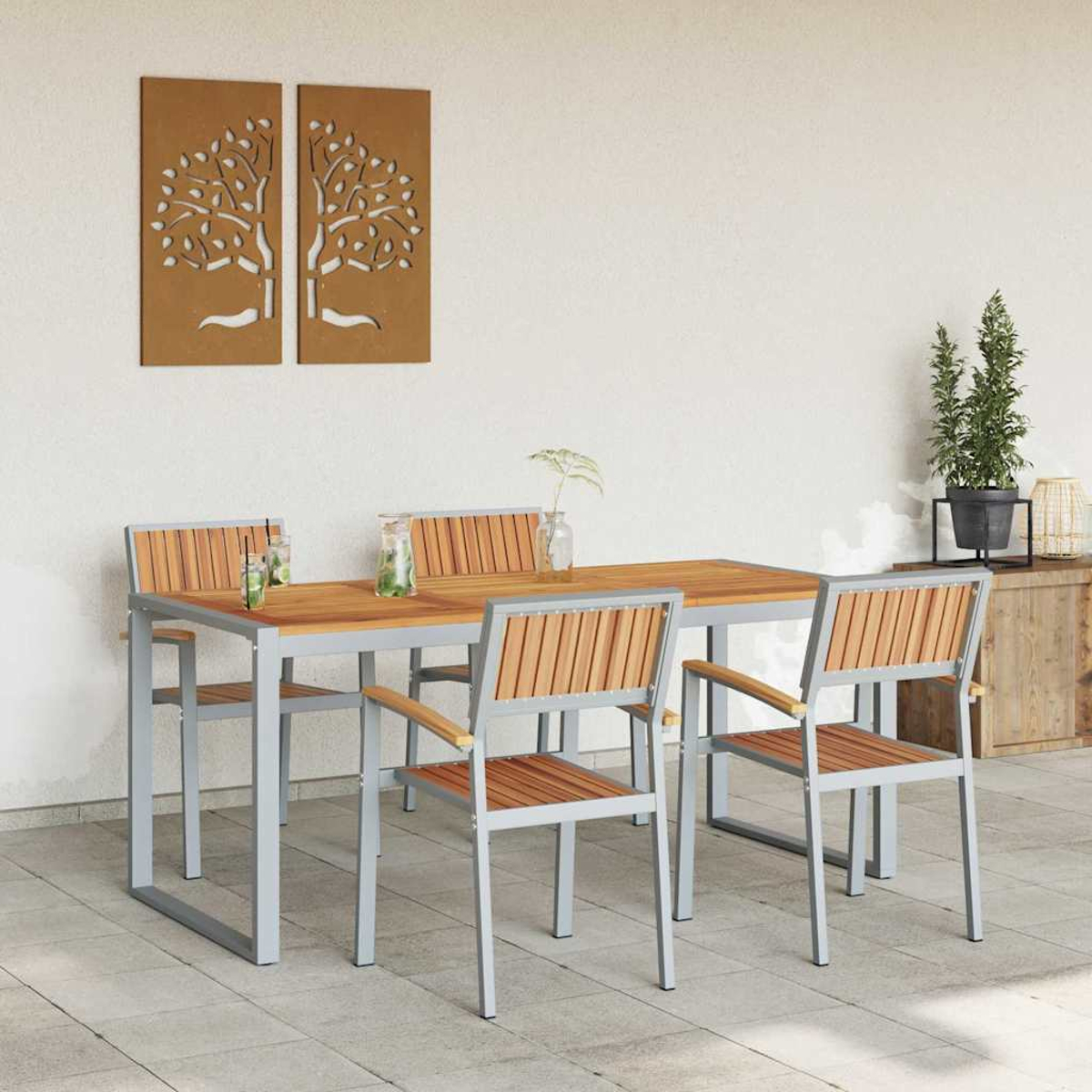 Juego de comedor al aire libre con mesa y sillas de madera. Paneles decorativos de árboles cuelgan en la pared blanca.