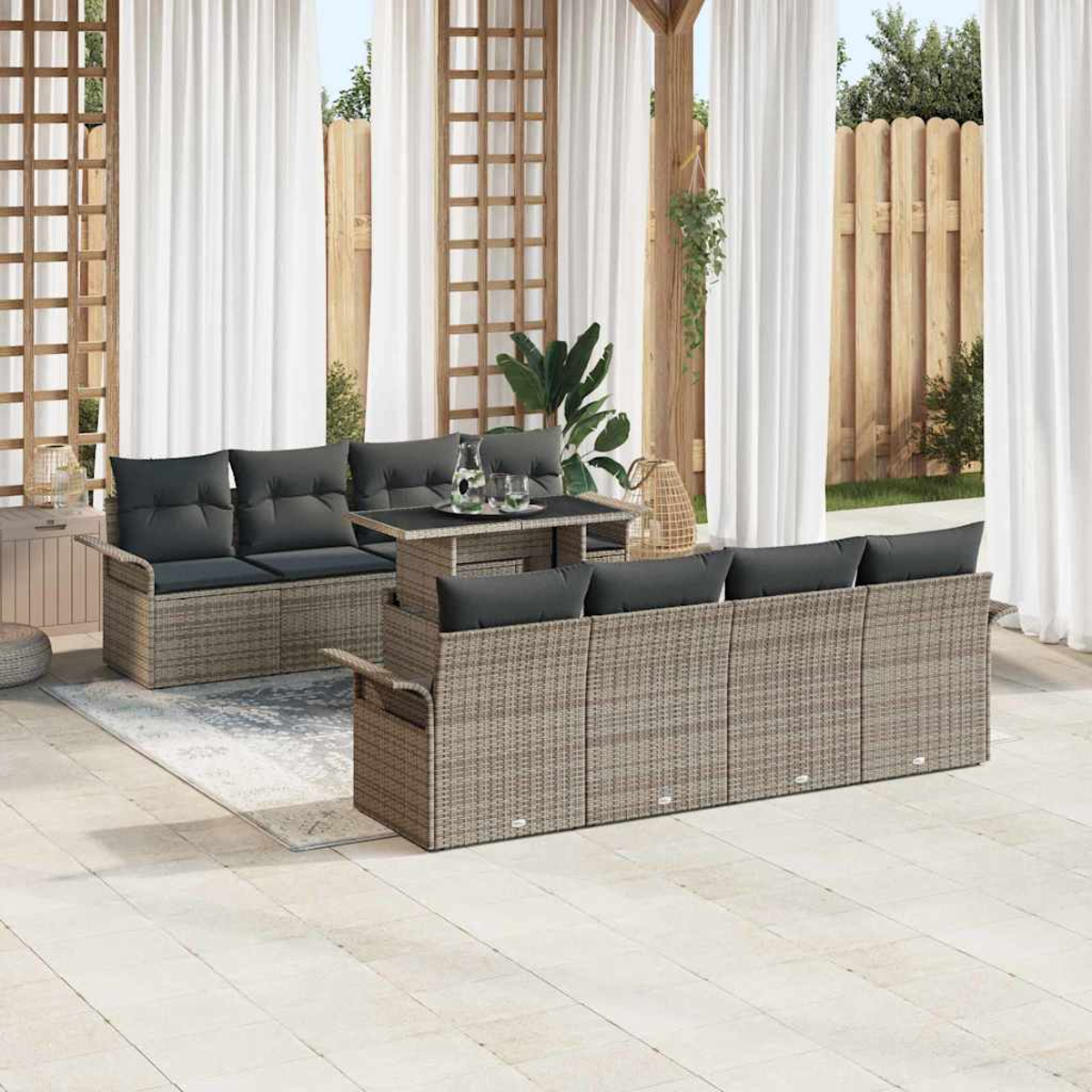 Garten-Terrassenset mit grauen Kissen, Tisch und Pflanzen. Weiße Vorhänge und Holzzaun im Hintergrund. Sonniger Tag.