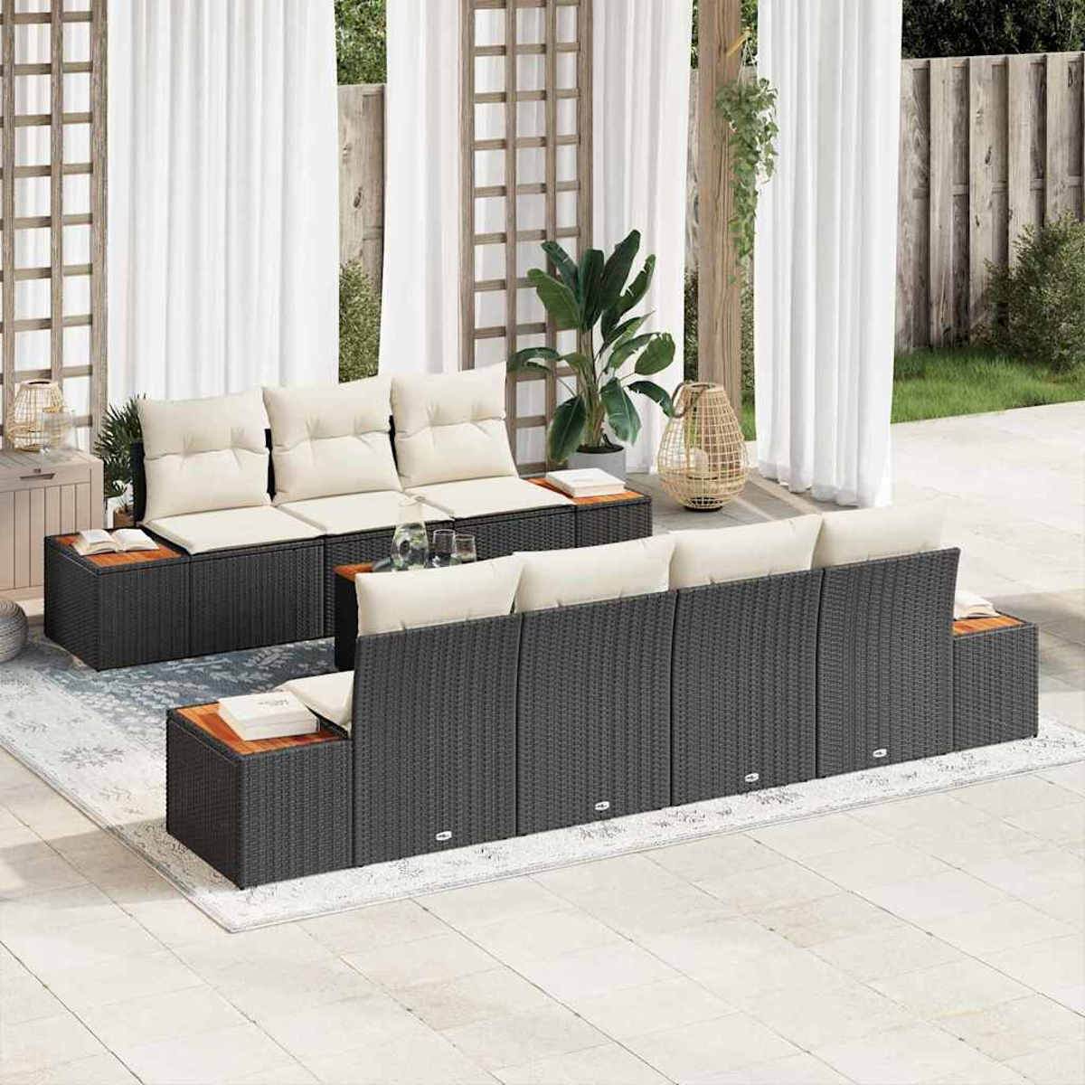 Garten-Sitzgruppe mit dunkelgrauem Korbgeflecht, beigen Kissen und Holzplatten, auf einer Terrasse mit weißen Vorhängen und Pflanzen.
