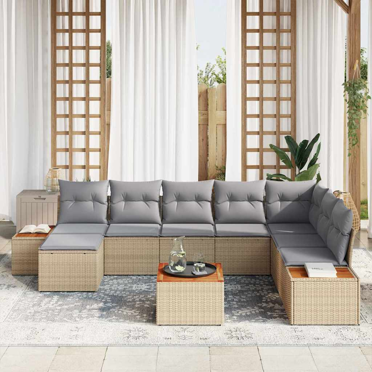 Sofá seccional exterior con cojines grises, dos mesas cuadradas, cortinas blancas y una alfombra. El fondo muestra una ventana y plantas.
