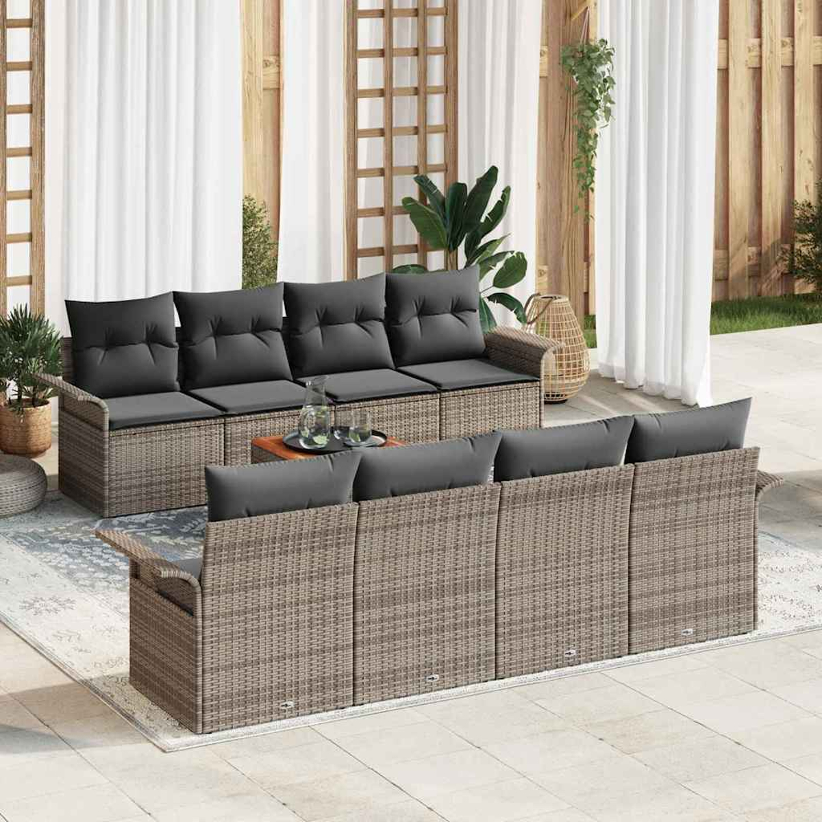 Juego de muebles de patio al aire libre con cojines grises. Una mesa con bebidas se encuentra entre los dos sofás. Cortinas blancas y plantas al fondo.