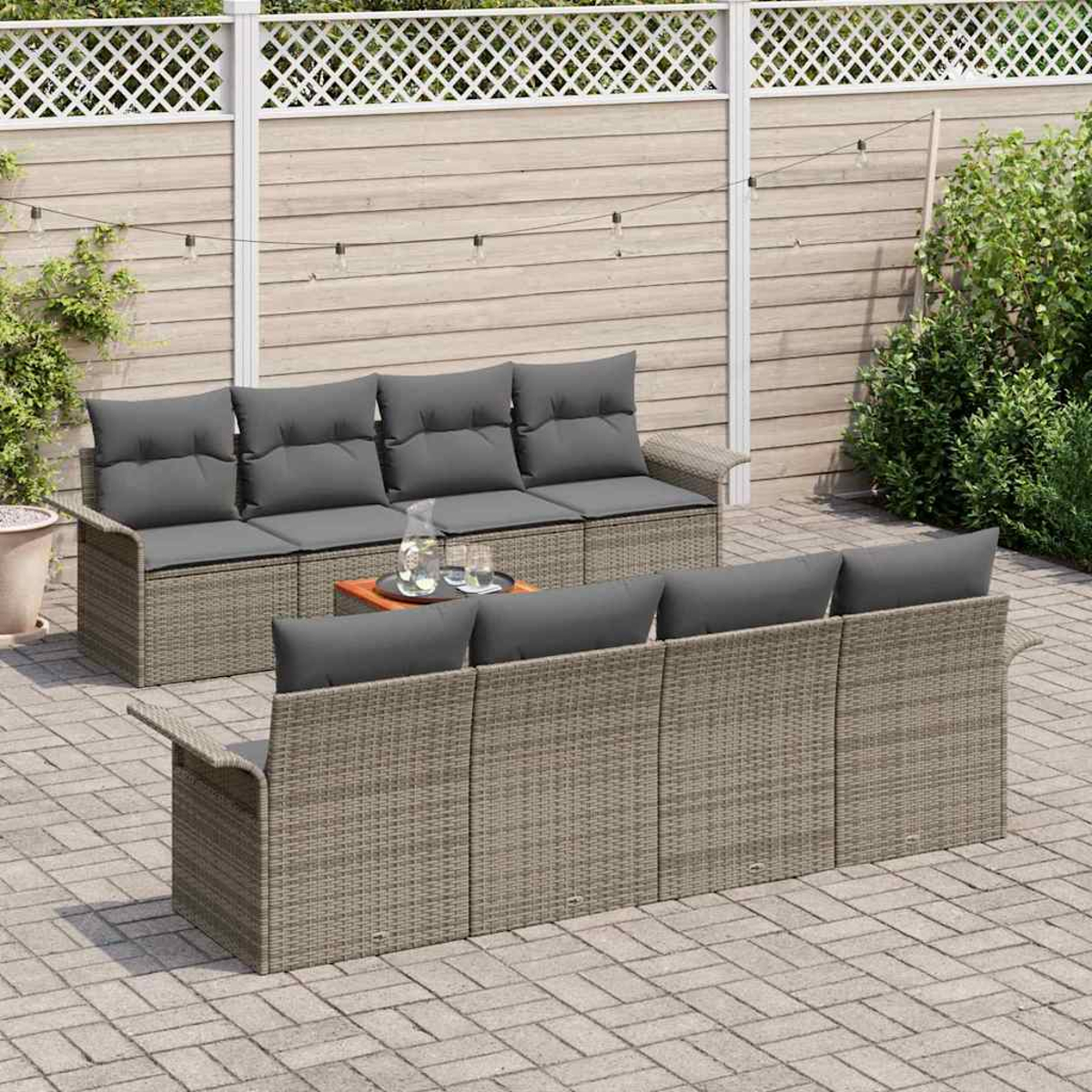 Juego de patio al aire libre con cojines grises. Una mesa pequeña con bebidas en el medio. Valla de madera y vegetación al fondo.