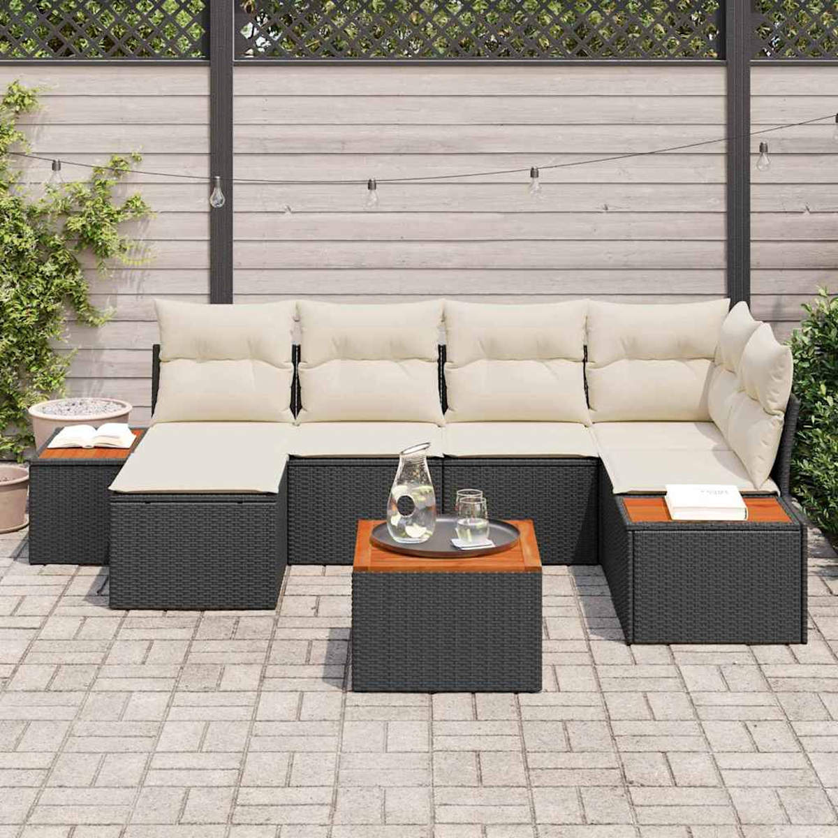 Outdoor-Ecksofa mit cremefarbenen Kissen und einem Holztisch. Wasserkrug und Gläser auf dem Tisch. Graues Korbgeflecht mit Holzakzenten.