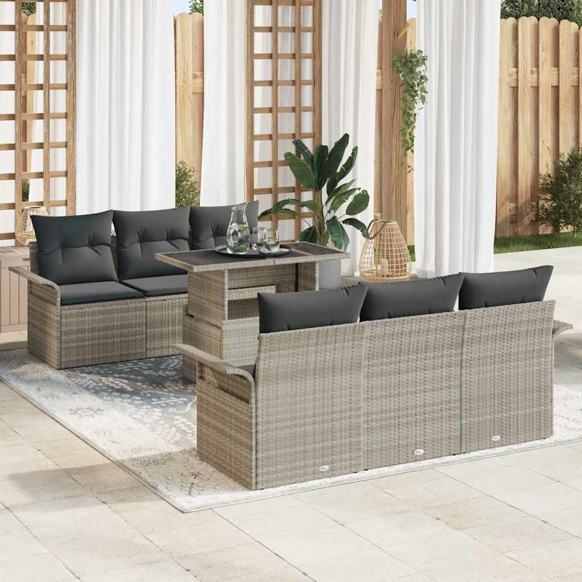 Garten-Sitzgruppe auf einer Terrasse. Enthält Tisch, zwei Sofas mit dunklen Kissen und einen Teppich. Vorhänge und Holzzaun im Hintergrund.