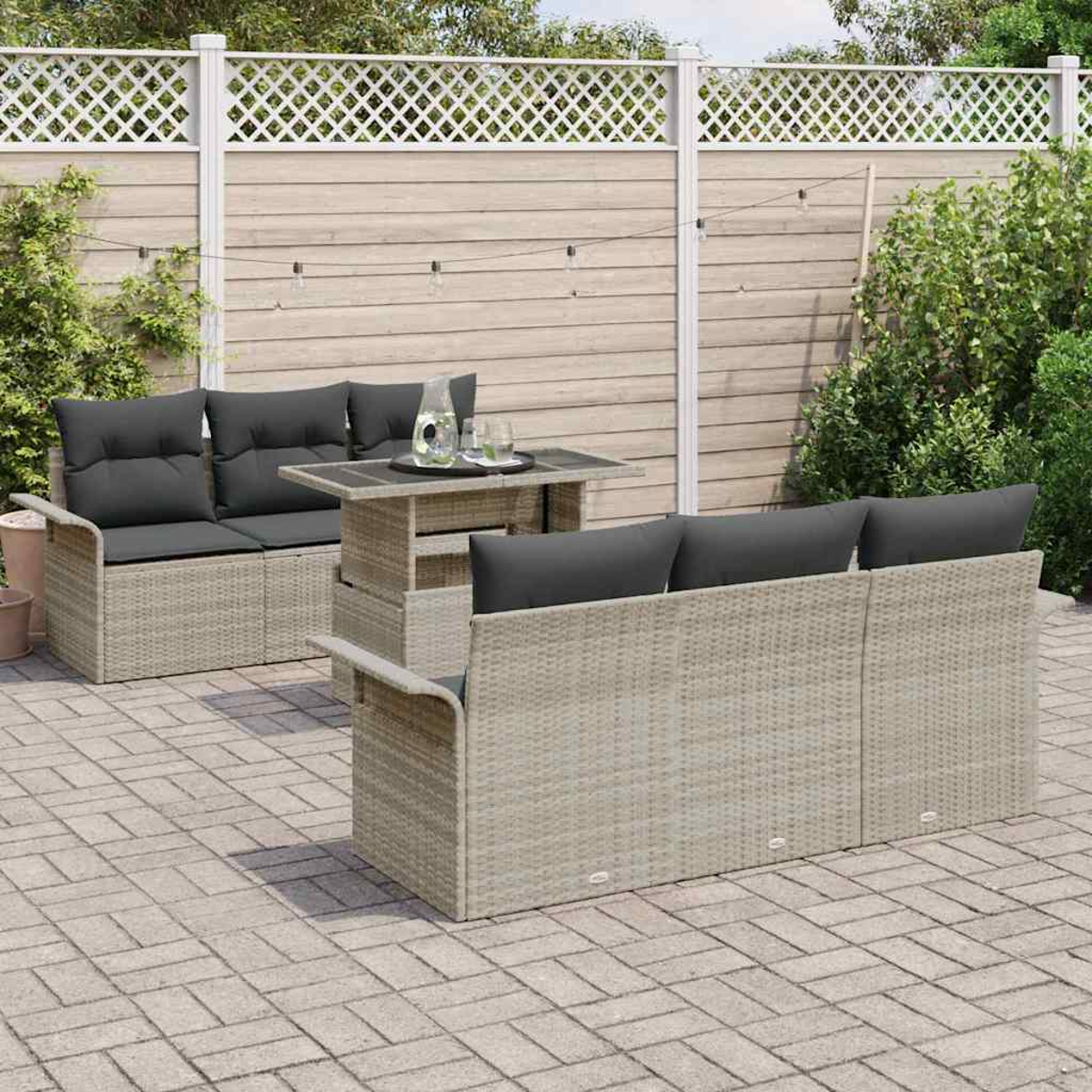 Gartenmöbel-Set auf einer Terrasse. Enthält Sofa, Liebesitz und Tisch mit Getränken, vor einem Zaun und Büschen.