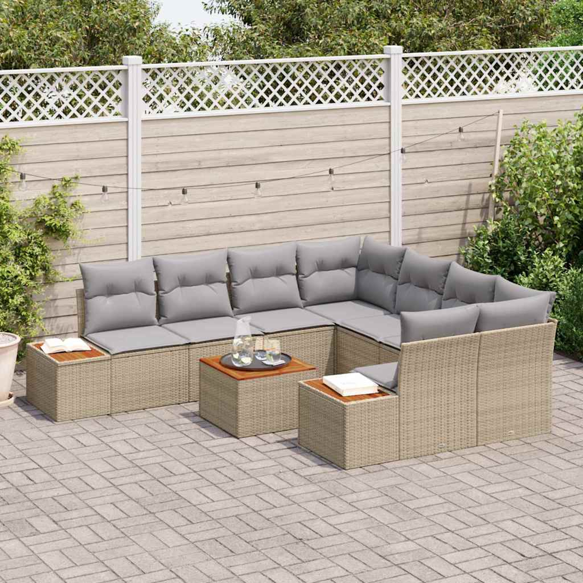 Sofá seccional de ratán para exteriores con cojines grises y pequeñas mesas de madera. En un patio con valla blanca al fondo.