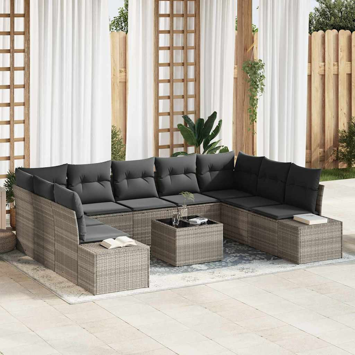 Outdoor-Ecksofa mit grauen Kissen, einem kleinen Tisch und einem Buch. Hintergrund: weiße Vorhänge und Holzzaun.