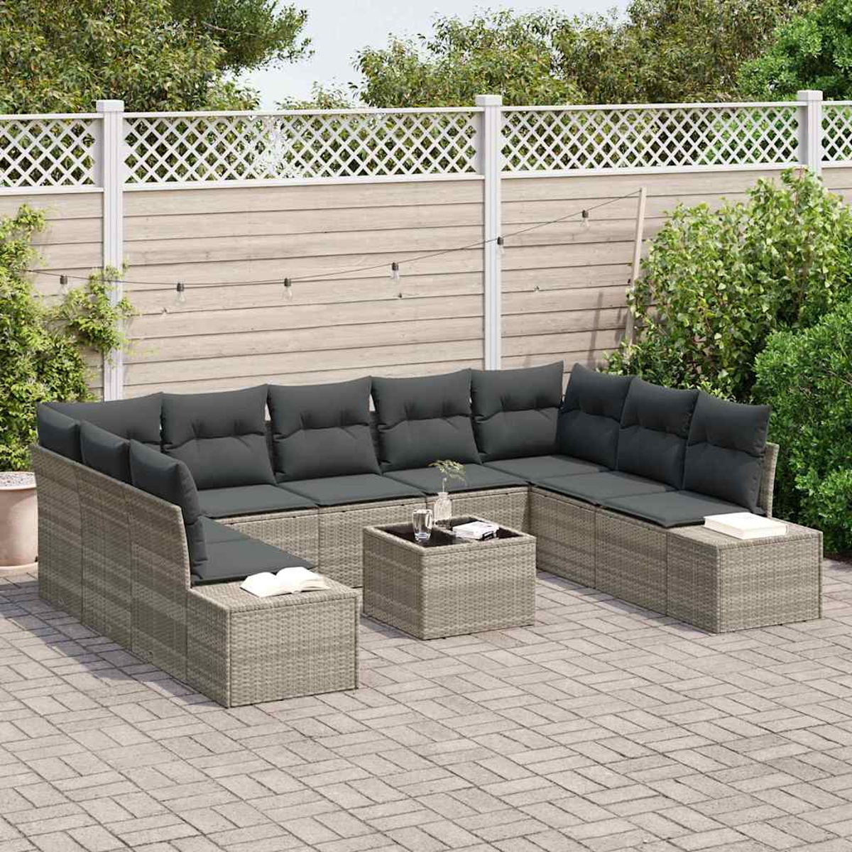 Graues Outdoor-Geflecht-Ecksofa mit dunkelgrauen Kissen, Couchtisch mit Glasplatte und weißem Zaun im Hintergrund.