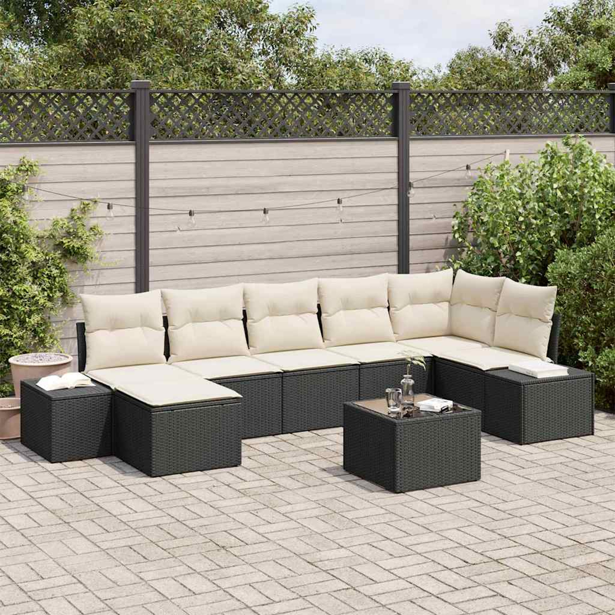Outdoor-Ecksofa mit hellen Kissen, schwarzem Korbgeflecht und kleinem Tisch. Dahinter ein Zaun und Grün.