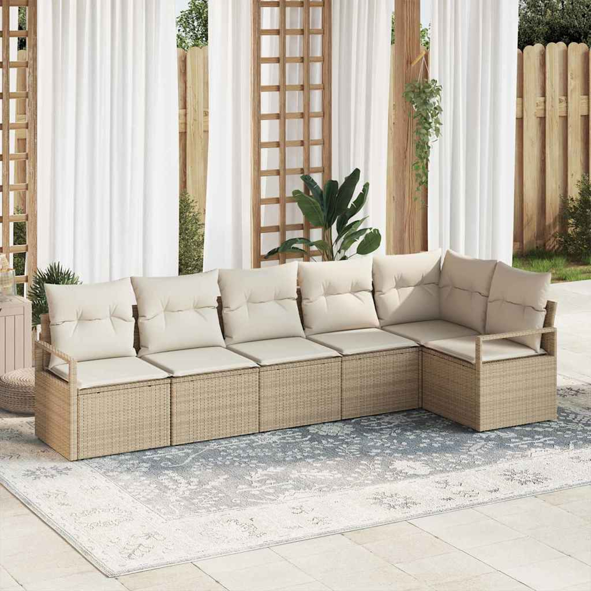 Beige Rattan-Sofa mit cremefarbenen Kissen auf einem gemusterten Teppich. Dahinter weiße Vorhänge, Holzgitter und Pflanzen.