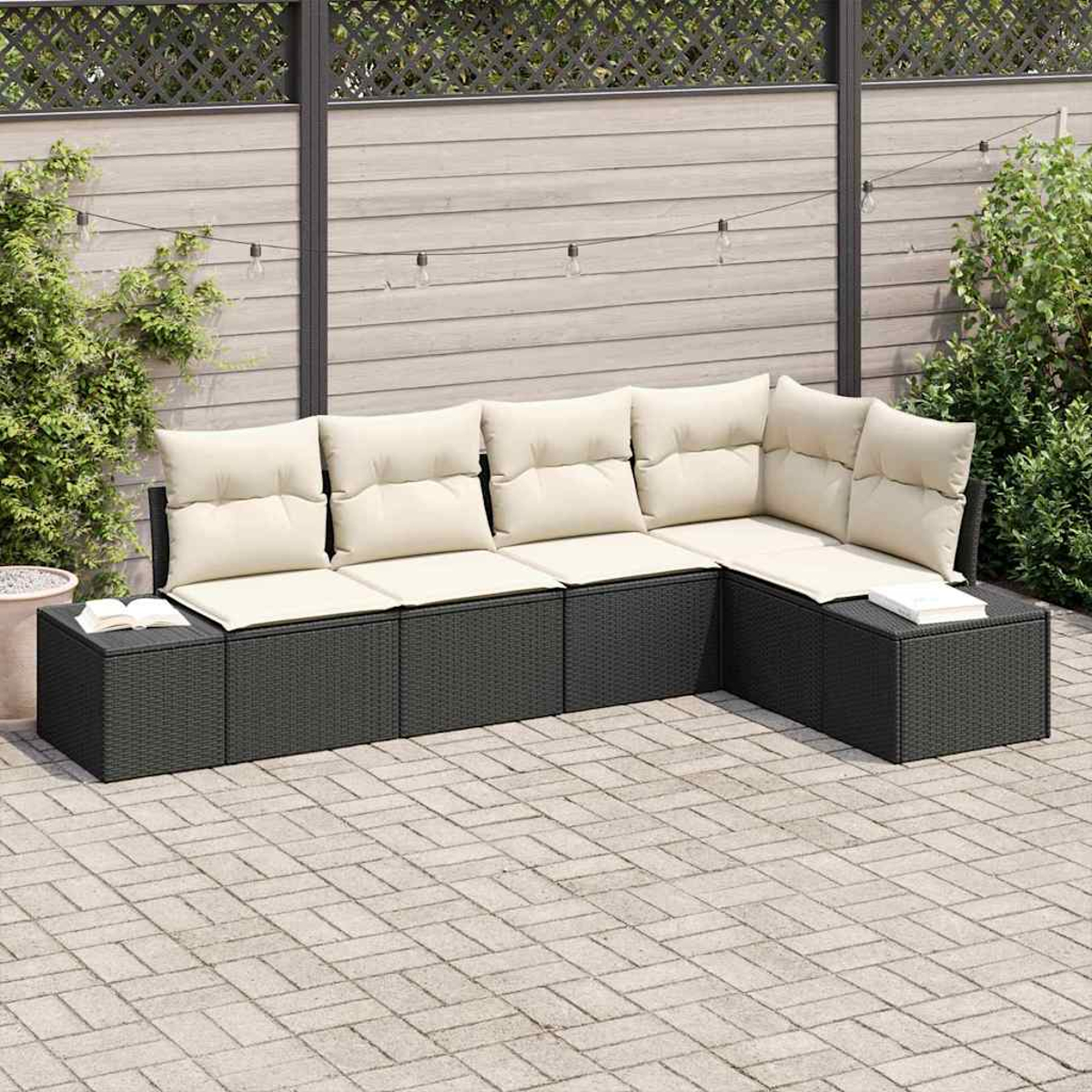 Ein Ecksofa im Freien mit beigefarbenen Kissen auf einer Ziegelterrasse. Ein Holzzaun im Hintergrund mit Lichterketten und Grün.