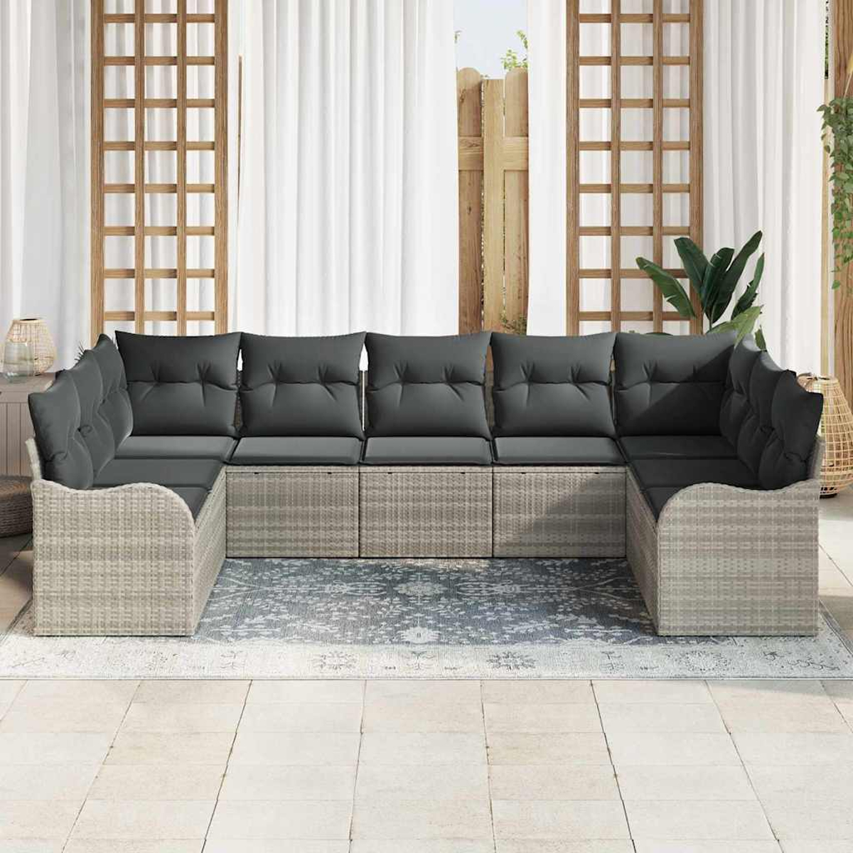 U-förmiges Sofa im Freien mit grauen Kissen, auf einem gemusterten Teppich. Transparente Vorhänge und Holzgitter im Hintergrund.