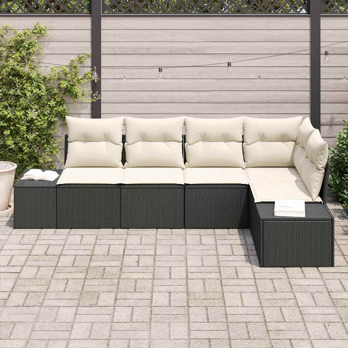 Outdoor-Ecksofa mit cremefarbenen Kissen auf grauem Korbgeflecht. Es steht auf einer Ziegelterrasse mit Holzzaun im Hintergrund.