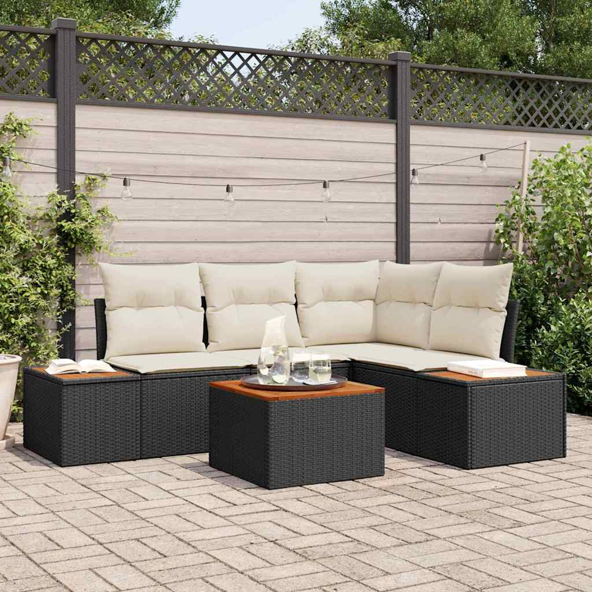 Garten-Terrassenset mit schwarzem Korbmöbel, beigen Kissen und einem Holztisch. Ein Zaun und Grünzeug sind im Hintergrund.