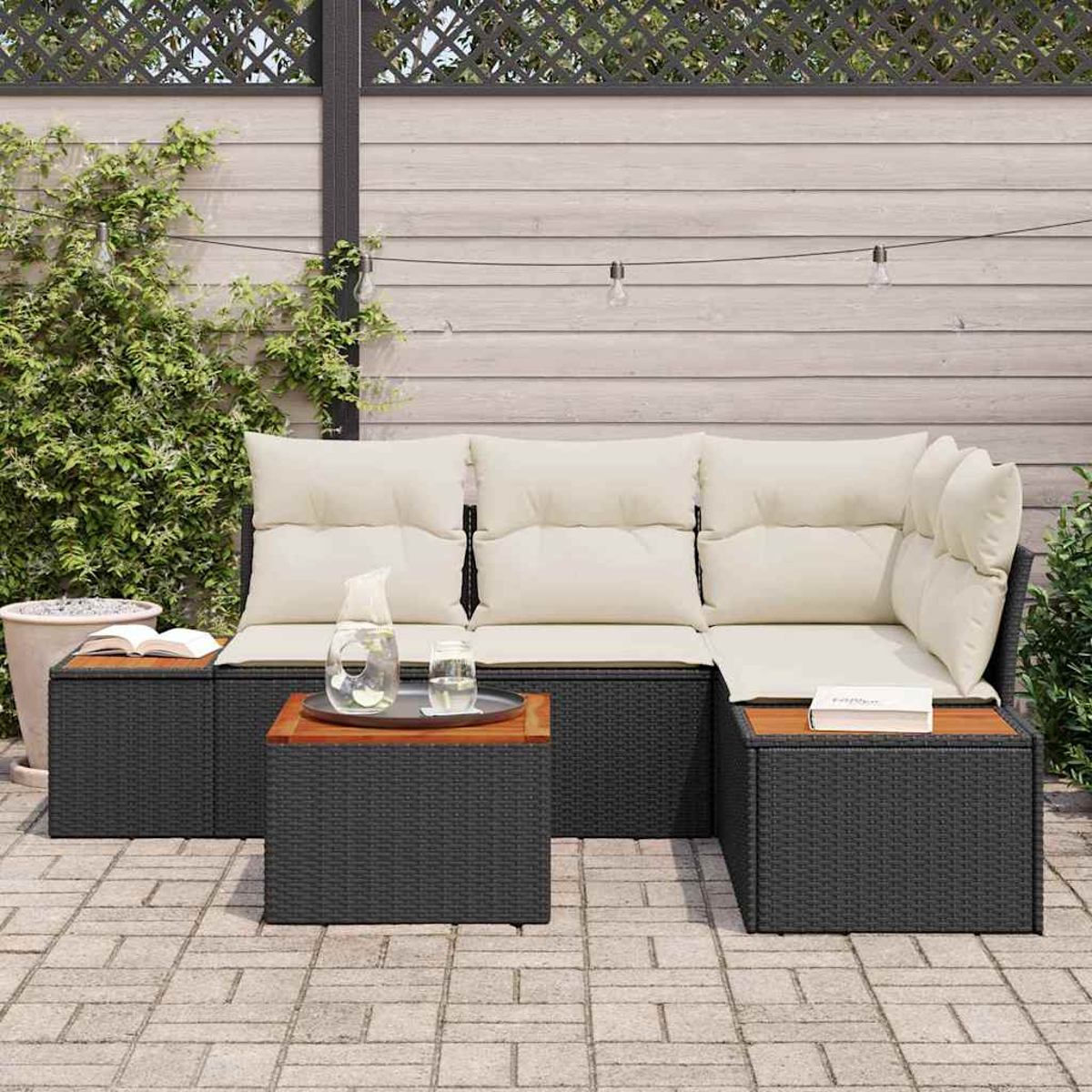 Terrassenset im Freien mit schwarzen gewebten Möbeln, cremefarbenen Kissen und Holztischplatten. Enthält eine Wasserkaraffe und Gläser.