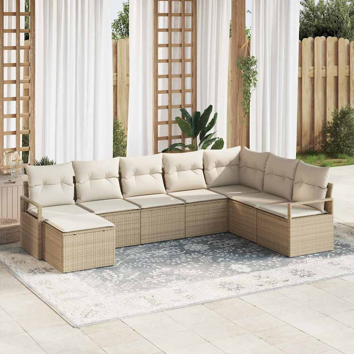 Ein beiges Rattan-Ecksofa mit cremefarbenen Kissen steht auf einem gemusterten Teppich. Weiße Vorhänge und Holzstrukturen sind im Hintergrund.