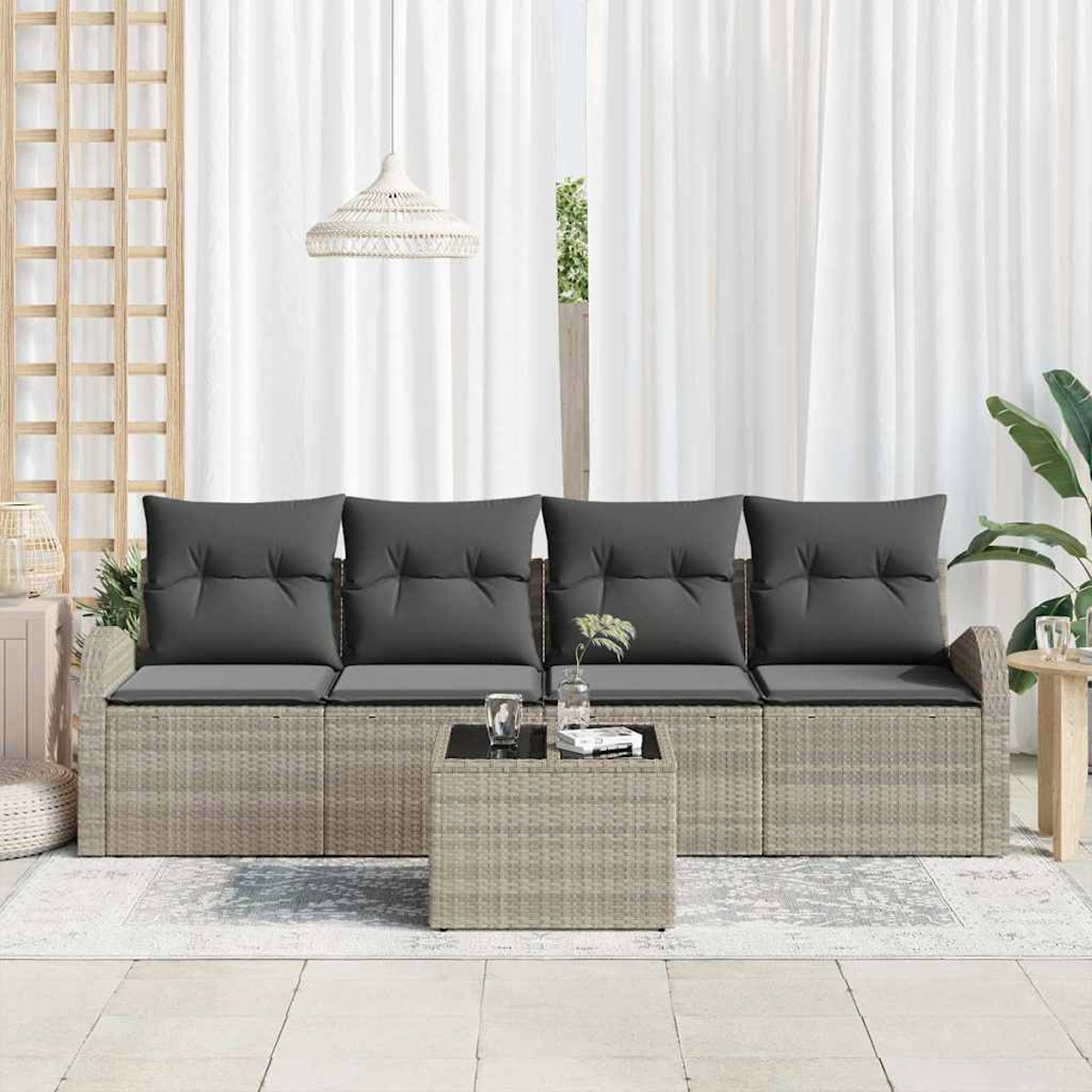 Garten-Sitzgruppe mit grauen Kissen, kleinem Tisch und weißen Vorhängen im Hintergrund. Rechts eine Pflanze.