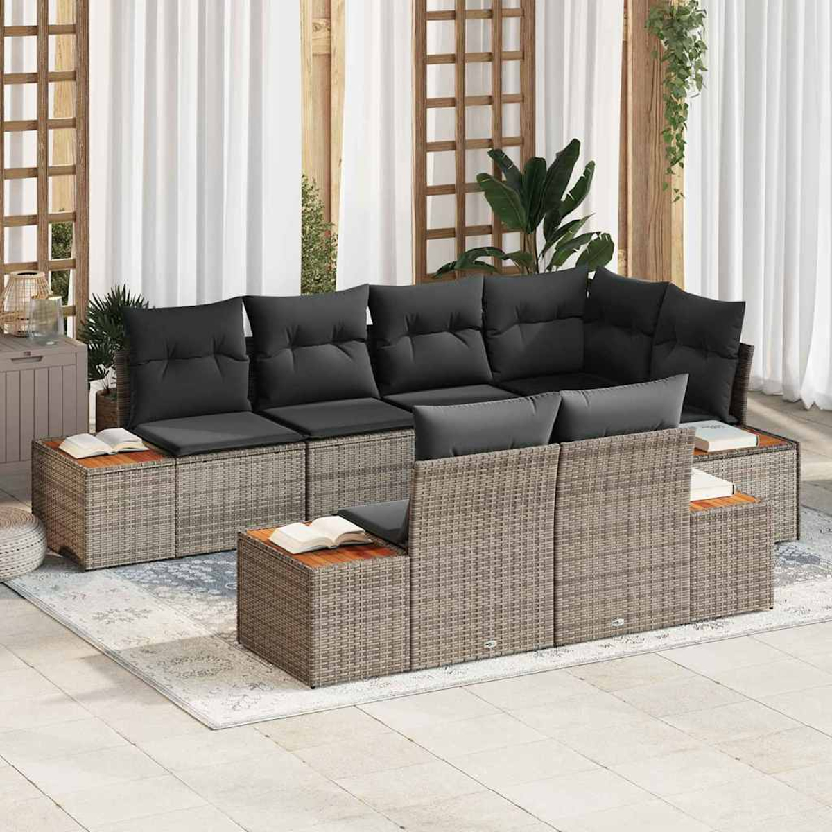 Juego de sofás de ratán para exteriores con cojines negros, mesas auxiliares de madera y una alfombra. Fondo con cortinas blancas, estructuras de madera y plantas.