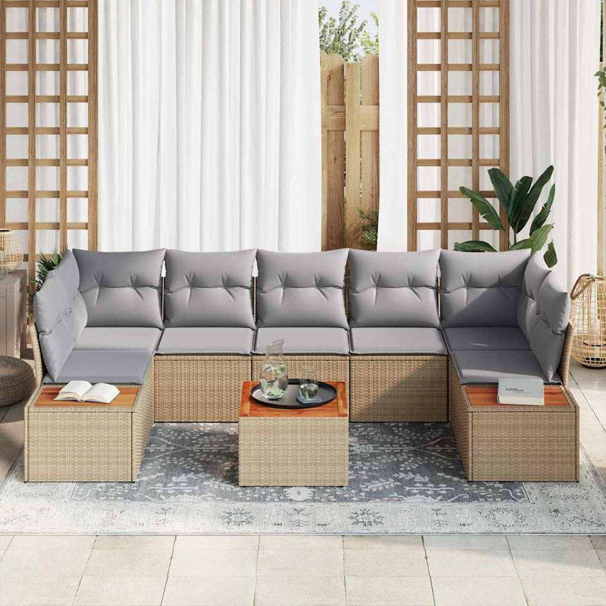 Outdoor-Ecksofa mit grauen Kissen und Rattangrundlage, auf einem gemusterten Teppich. Enthält zwei kleine Tische mit Büchern und Tablett.