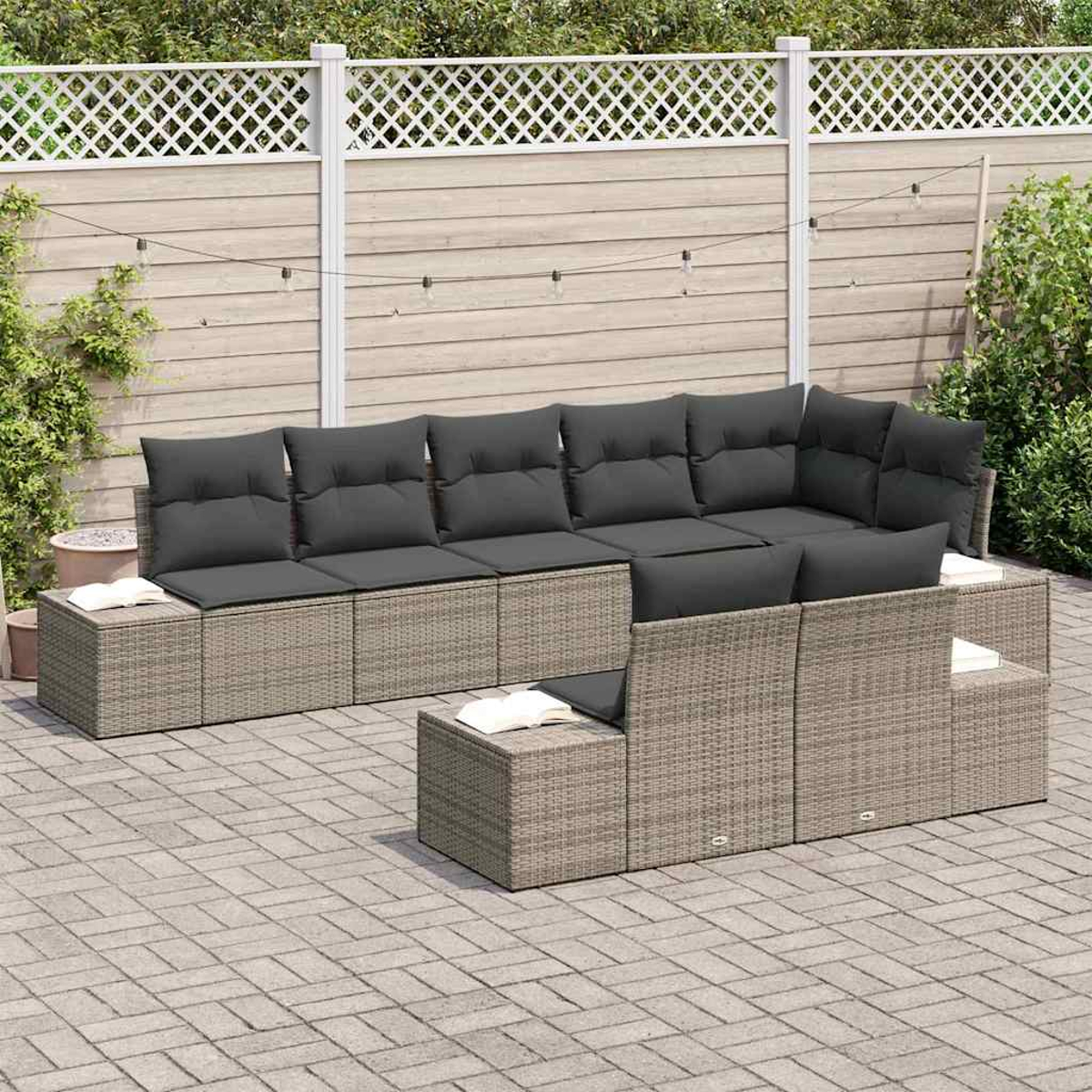 Juego de muebles de patio. Sofá de mimbre gris con cojines grises oscuros. Libros en las mesas laterales. Valla de madera y vegetación.