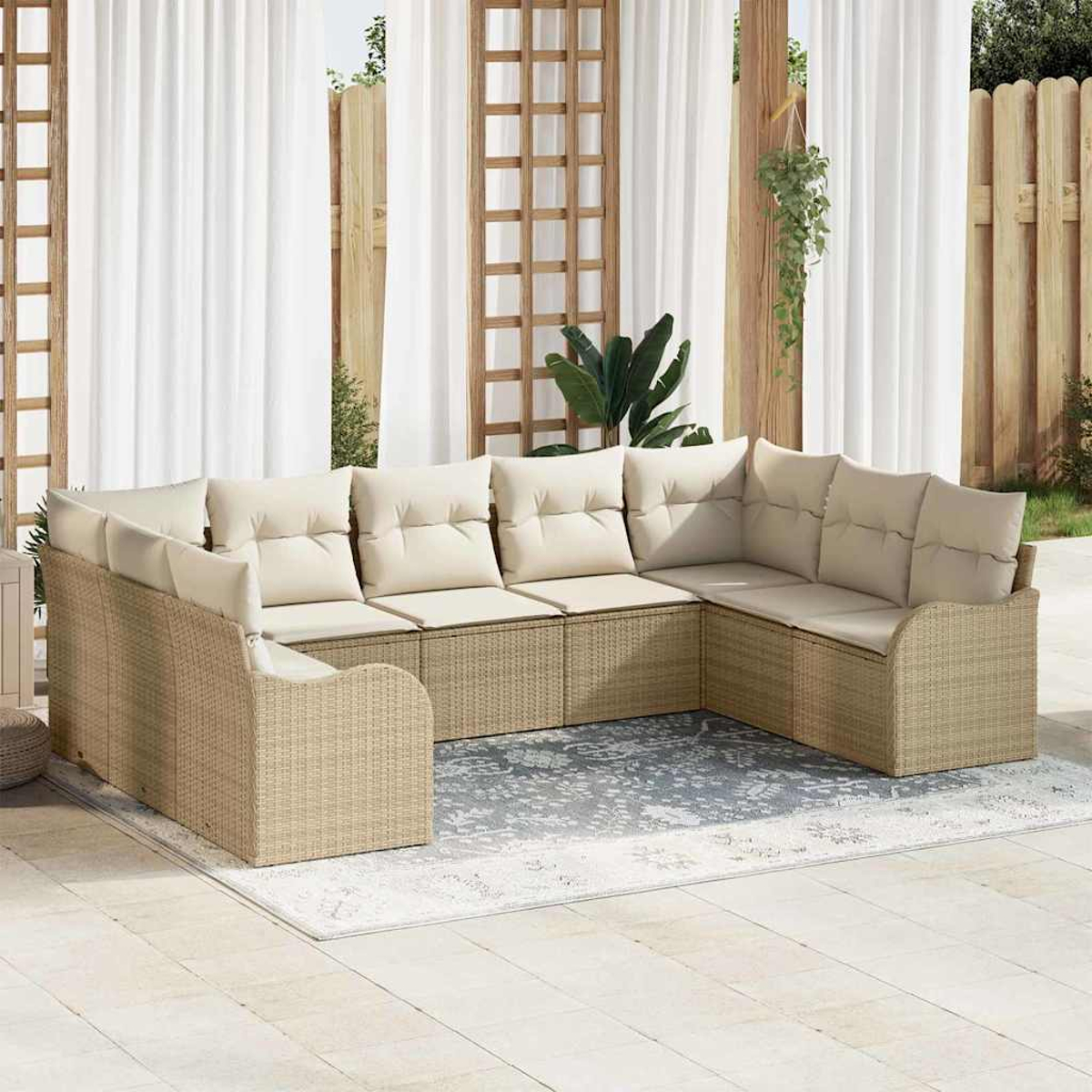 Beiges Outdoor-Rattansofa mit cremefarbenen Kissen auf einem gemusterten Teppich. Weiße Vorhänge und Holzzaun im Hintergrund.