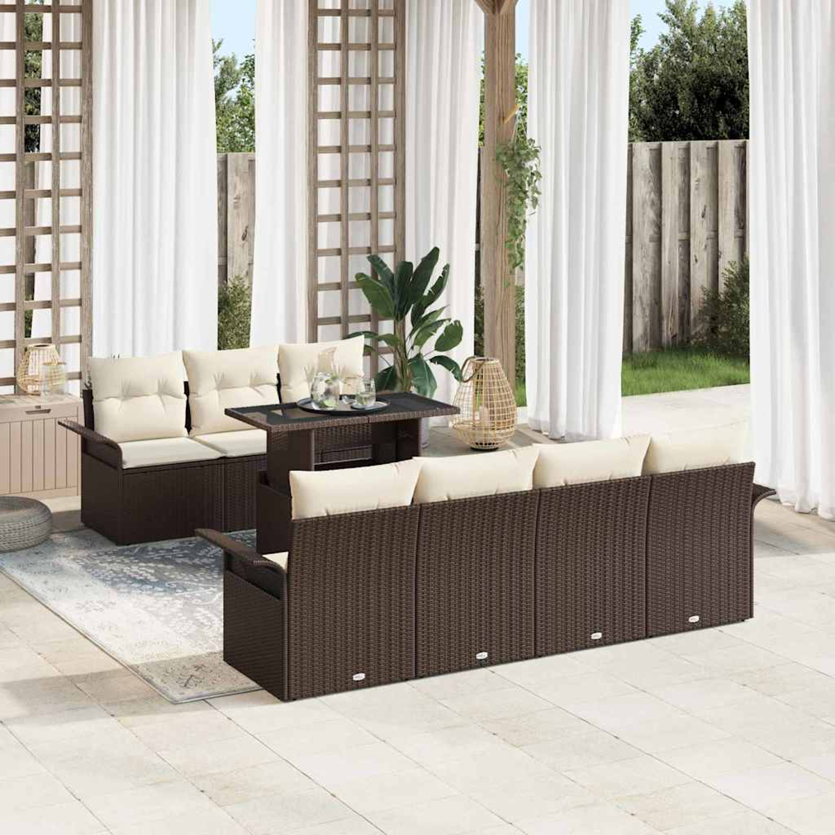 Terrassenset mit braunen Korbs Sofas, cremefarbenen Kissen, schwarzem Tisch. Weiße Vorhänge, Holzgitter im Hintergrund.