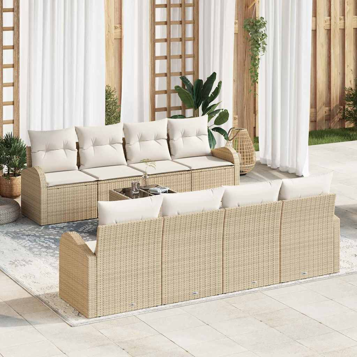 Außenbereich mit zwei Rattansofas, weißen Kissen und einem Glastisch. Weiße Vorhänge und Pflanzen im Hintergrund.