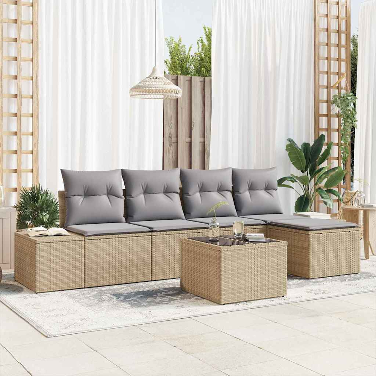 Outdoor-Rattansofa-Set mit grauen Kissen, Couchtisch und weißen Vorhängen im Hintergrund. Pflanzen und Holzelemente sind sichtbar.