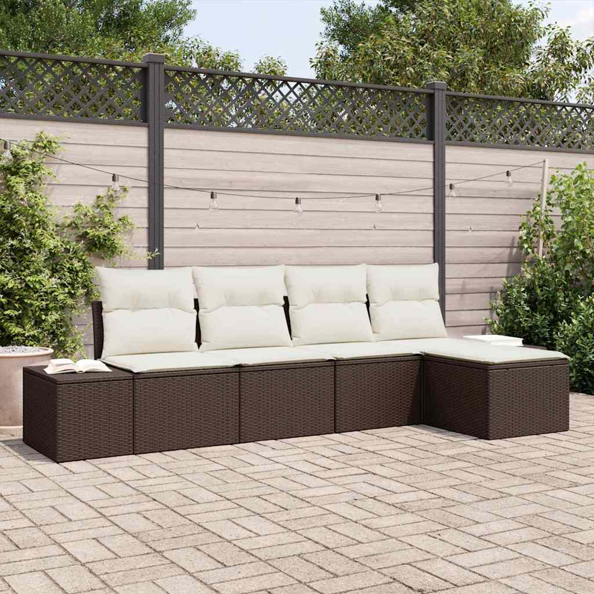 Braunes Ecksofa im Freien mit cremefarbenen Kissen. Auf einer Ziegelterrasse. Im Hintergrund ein Holzzaun mit Lichtern.