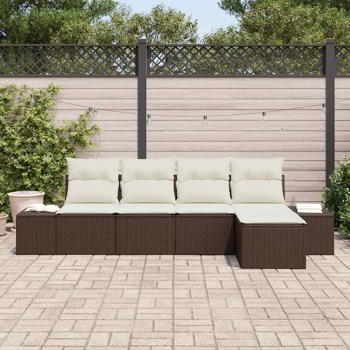 Outdoor-Ecksofa mit beigen Kissen. Braune Korbbasis. Der Hintergrund umfasst einen Holzzaun und Grün. Gepflasterte Terrasse.