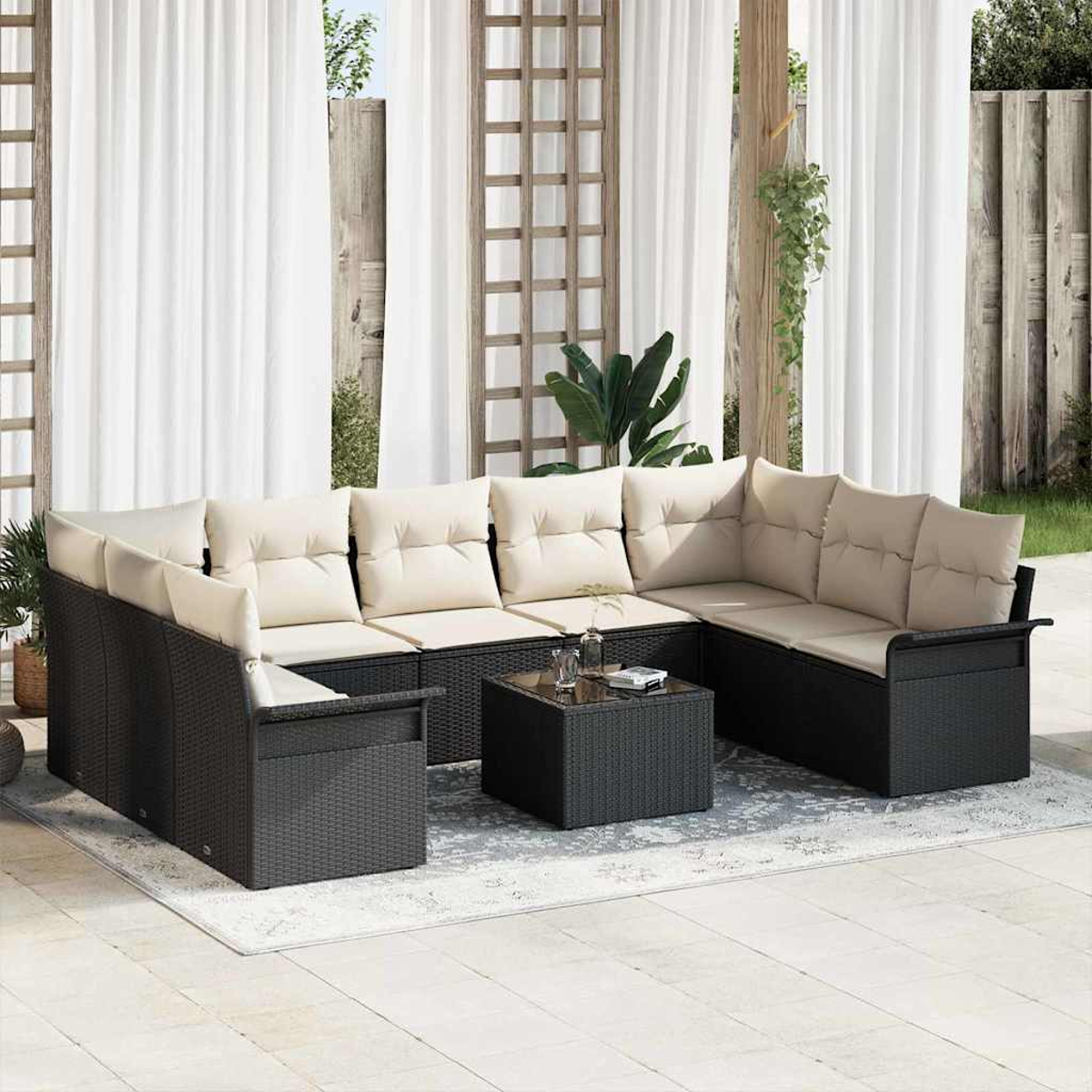 Garten-Sitzgruppe mit beigen Kissen, schwarzem Korbgewebe und kleinem Tisch. Weiße Vorhänge und hölzernes Spalier im Hintergrund.