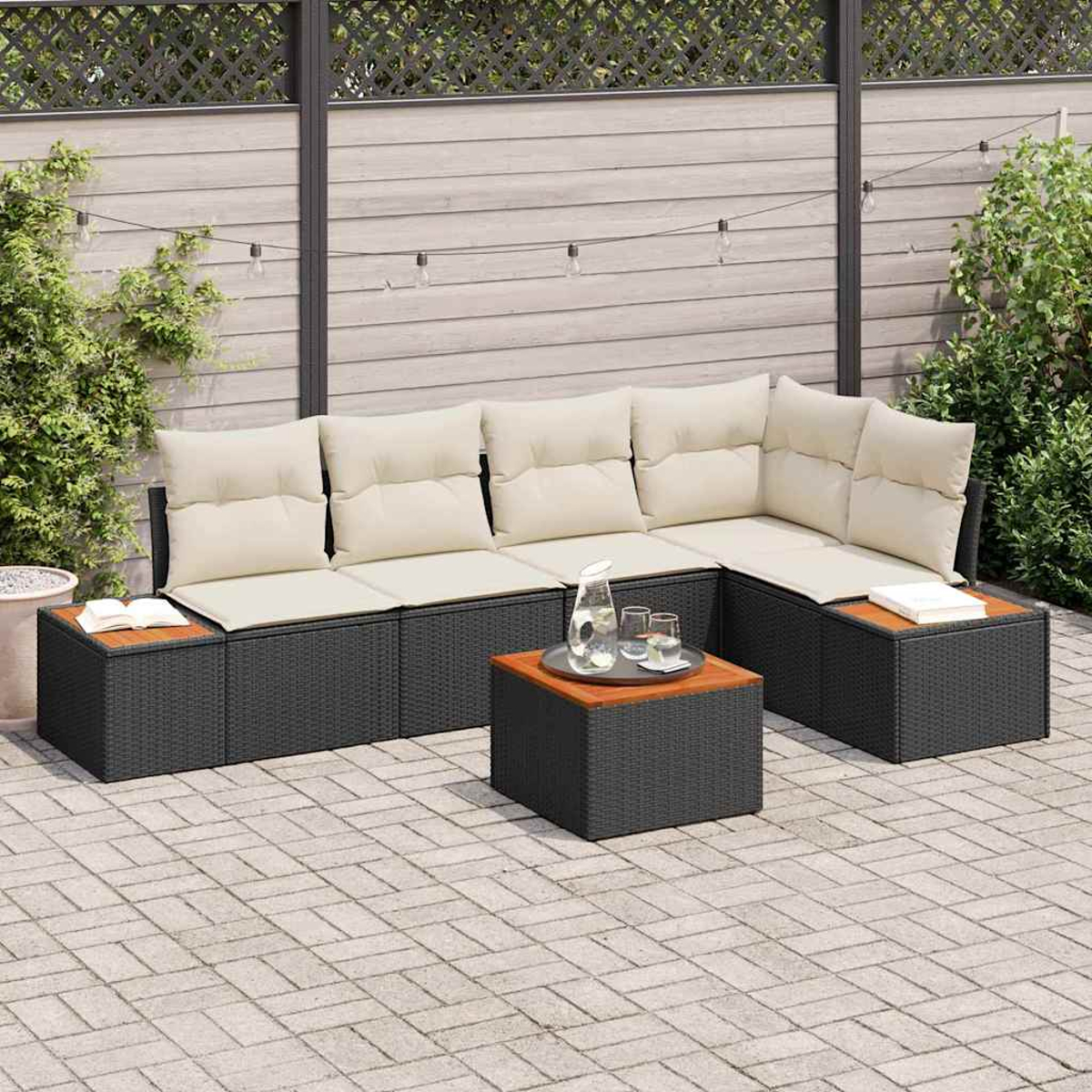 Outdoor-Ecksofa mit cremefarbenen Kissen, Couchtisch mit Gläsern und Lichterketten. Auf einer Steinterrasse mit Grün.