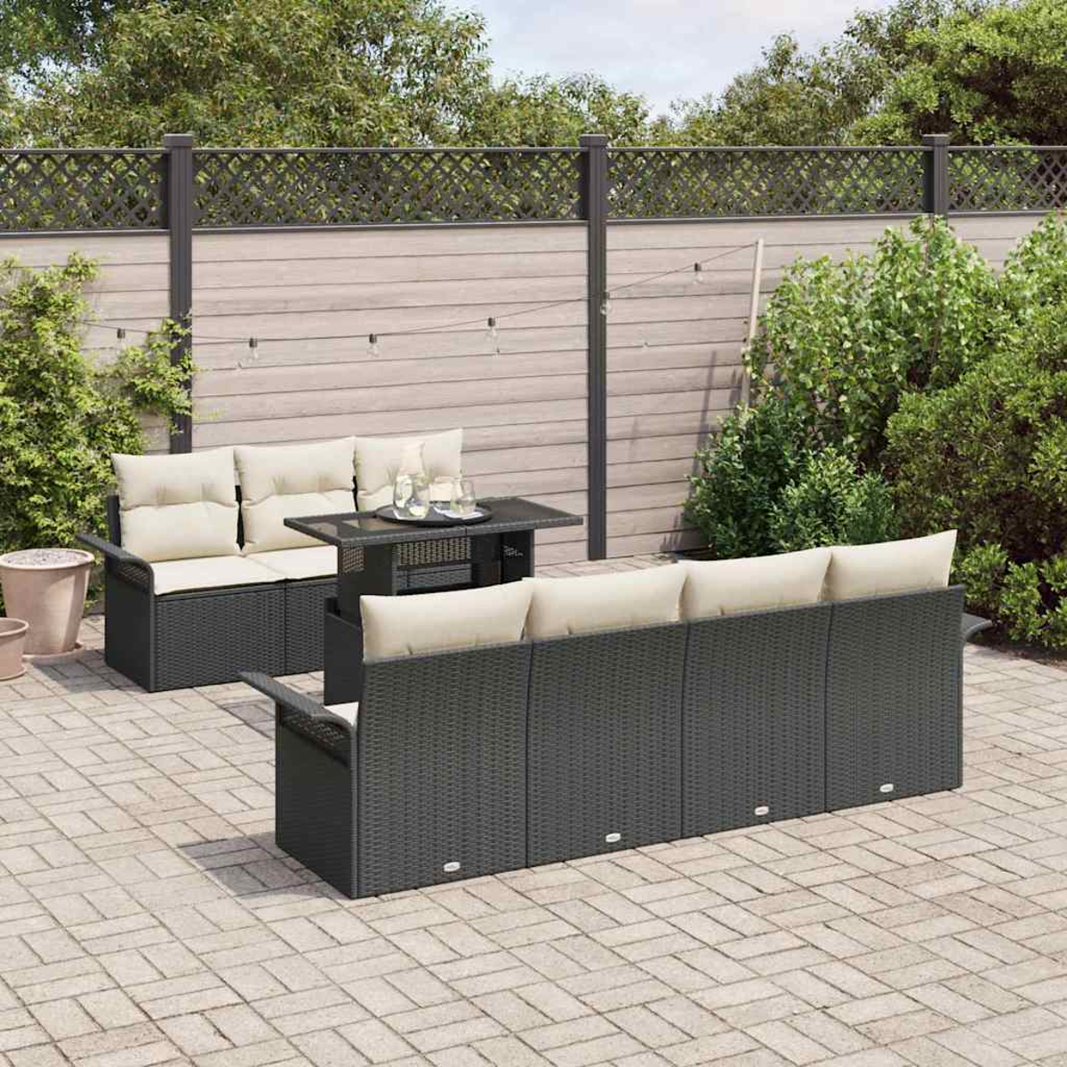 Set da patio all'aperto. Divano e divanetto in vimini grigio scuro con cuscini color crema, tavolino e recinzione in legno sullo sfondo.