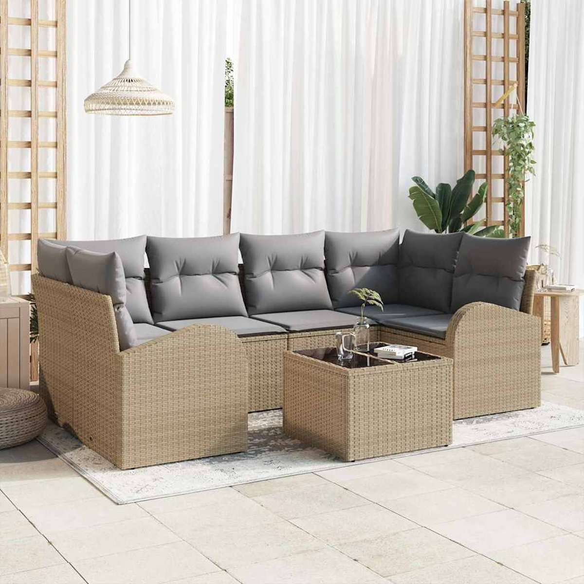Sofá seccional de mimbre para exteriores con cojines grises y mesa de centro. Cortinas blancas, una lámpara colgante y celosía de madera al fondo.