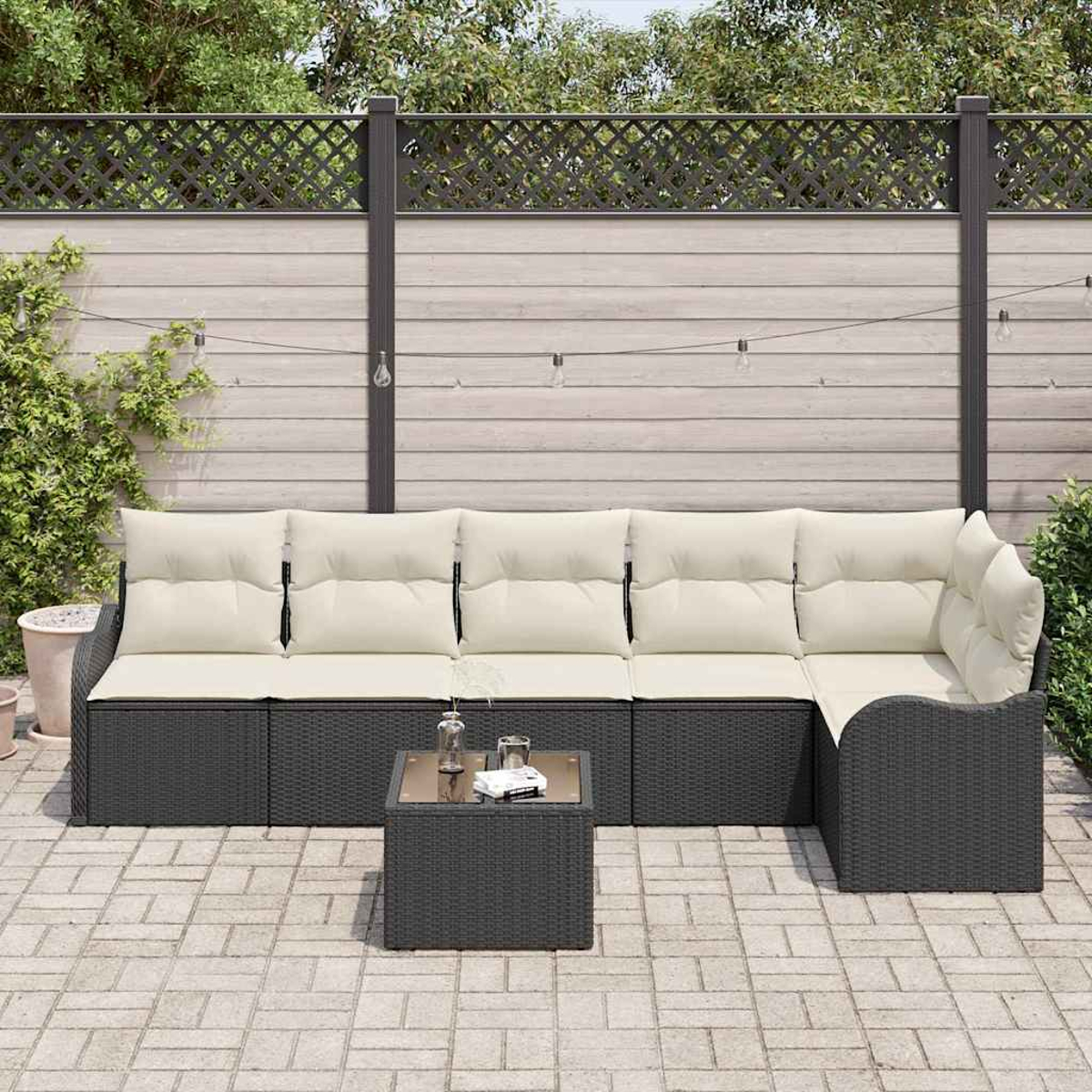 Sofá seccional para exteriores con cojines crema y una mesita en un patio de piedra. Una valla de madera y vegetación en el fondo.