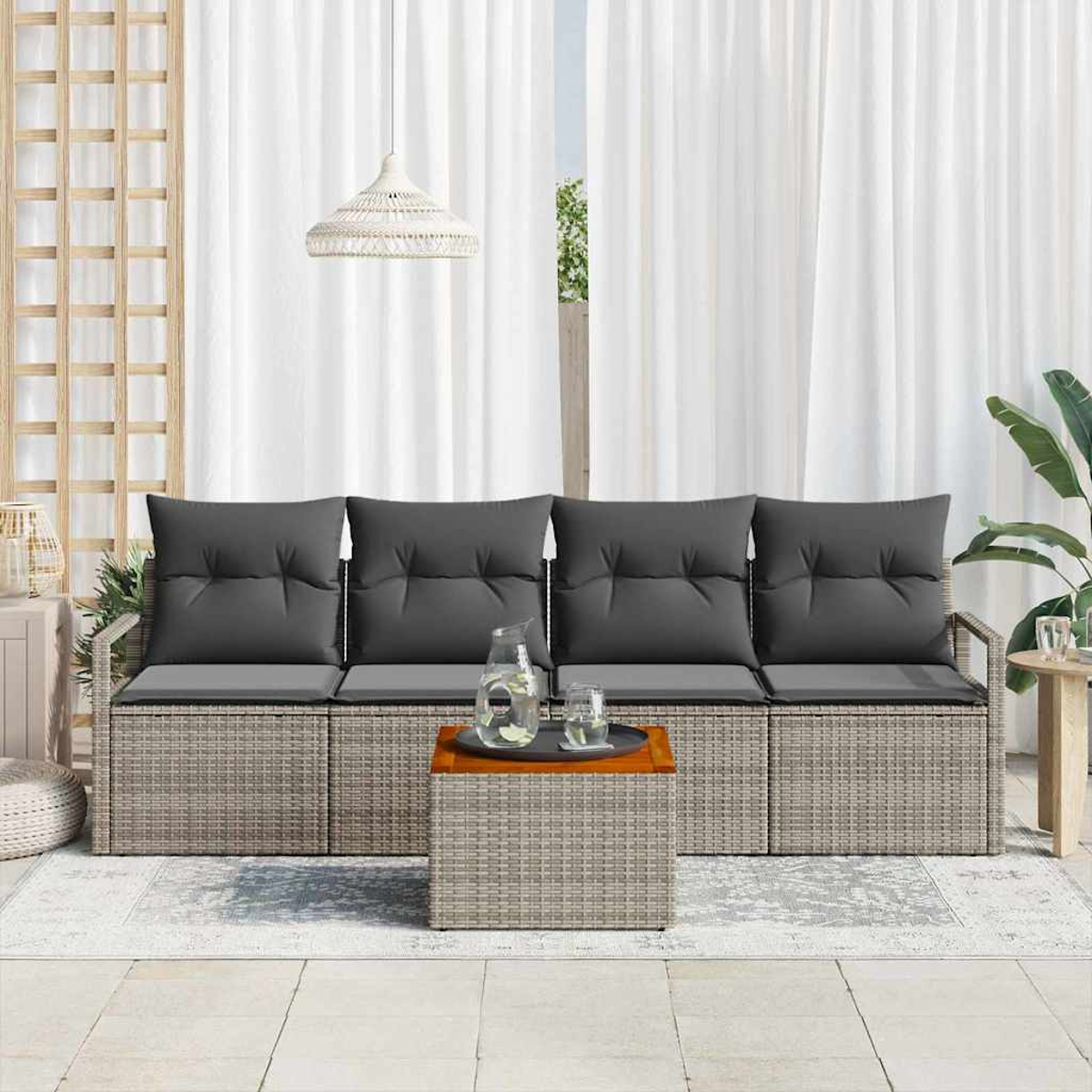 Escena al aire libre con un sofá gris tejido, cojines grises oscuros y una mesa de madera. Cortinas blancas de fondo.