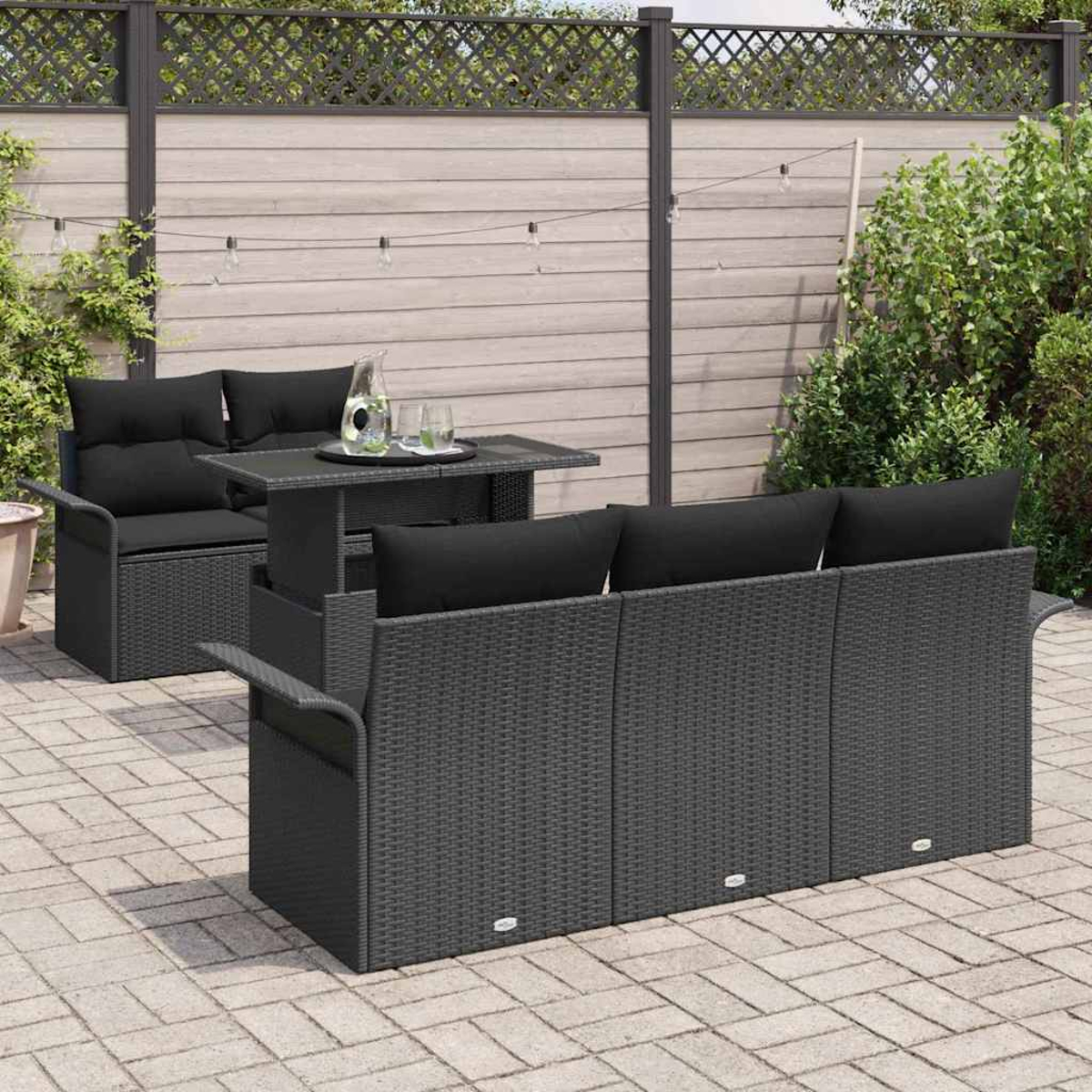 Gartenmöbel-Set. Dunkelgraues, gewebtes Sofa und Liebesitz mit schwarzen Kissen. Tisch mit Gläsern und einem Krug. Terrasse mit Pflanzen.