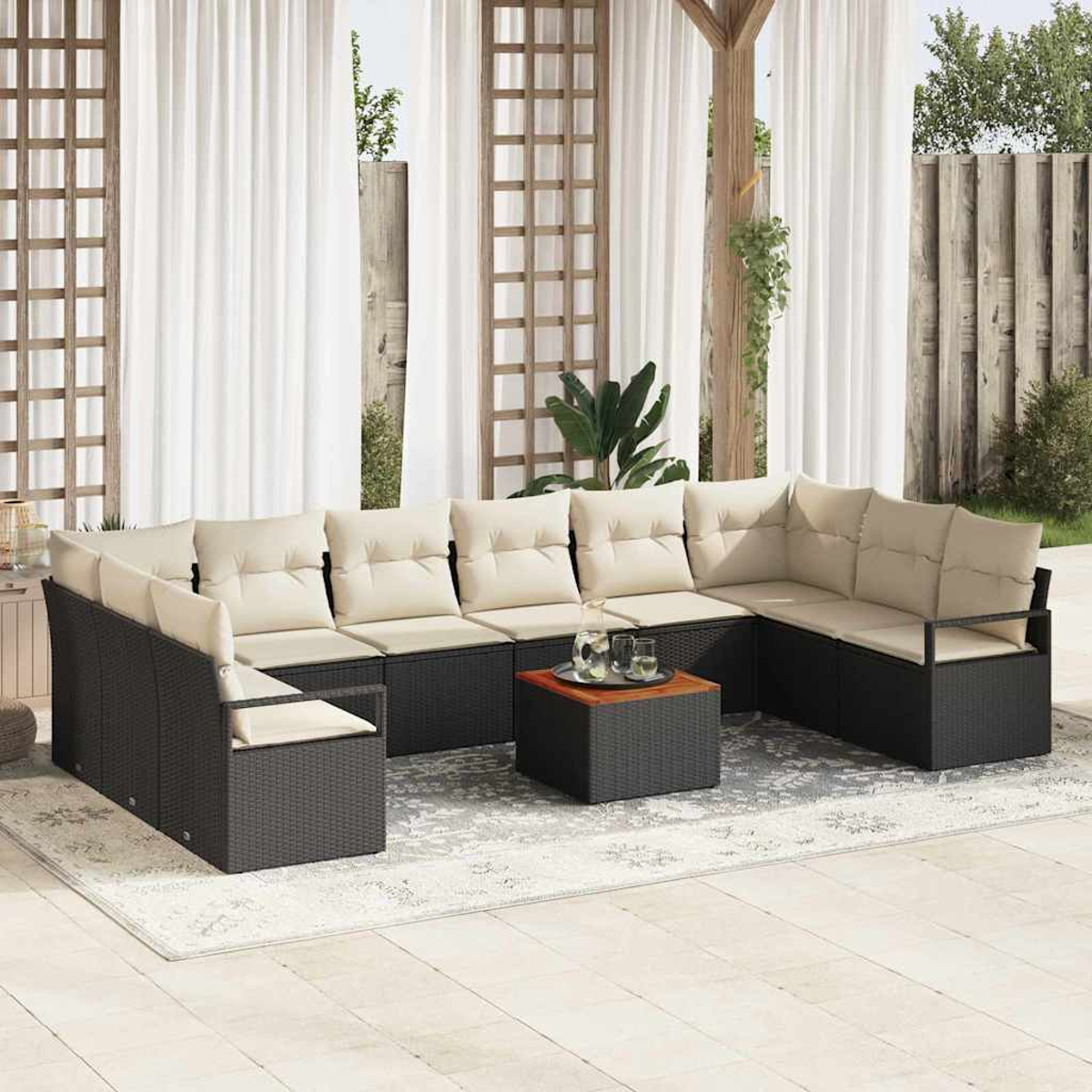 Sofá seccional exterior con cojines beige, una mesa pequeña con bebidas, cortinas blancas y un enrejado de madera al fondo.