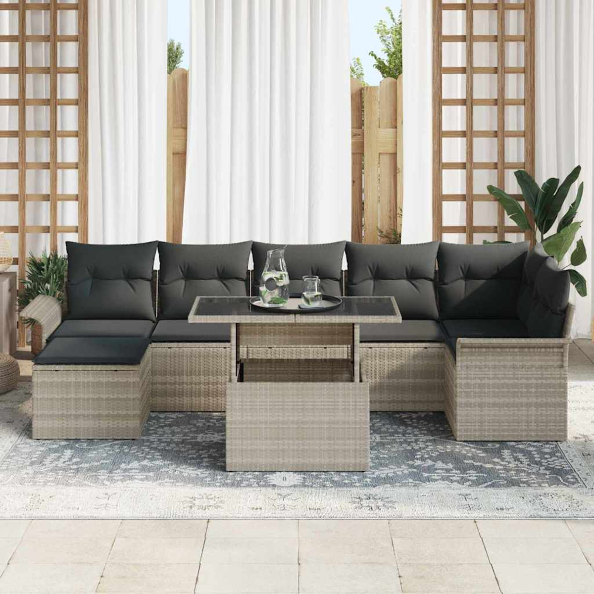 Outdoor-Ecksofa mit dunkelgrauen Kissen und einem Tisch mit Glasplatte. Weiße Vorhänge und ein gemusterter Teppich sind ebenfalls sichtbar.