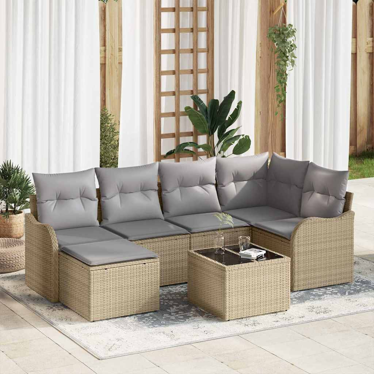 Outdoor-Rattan-Sofagarnitur mit grauen Kissen, Couchtisch mit Glasplatte, Pflanzen und weißen Vorhängen im Hintergrund.