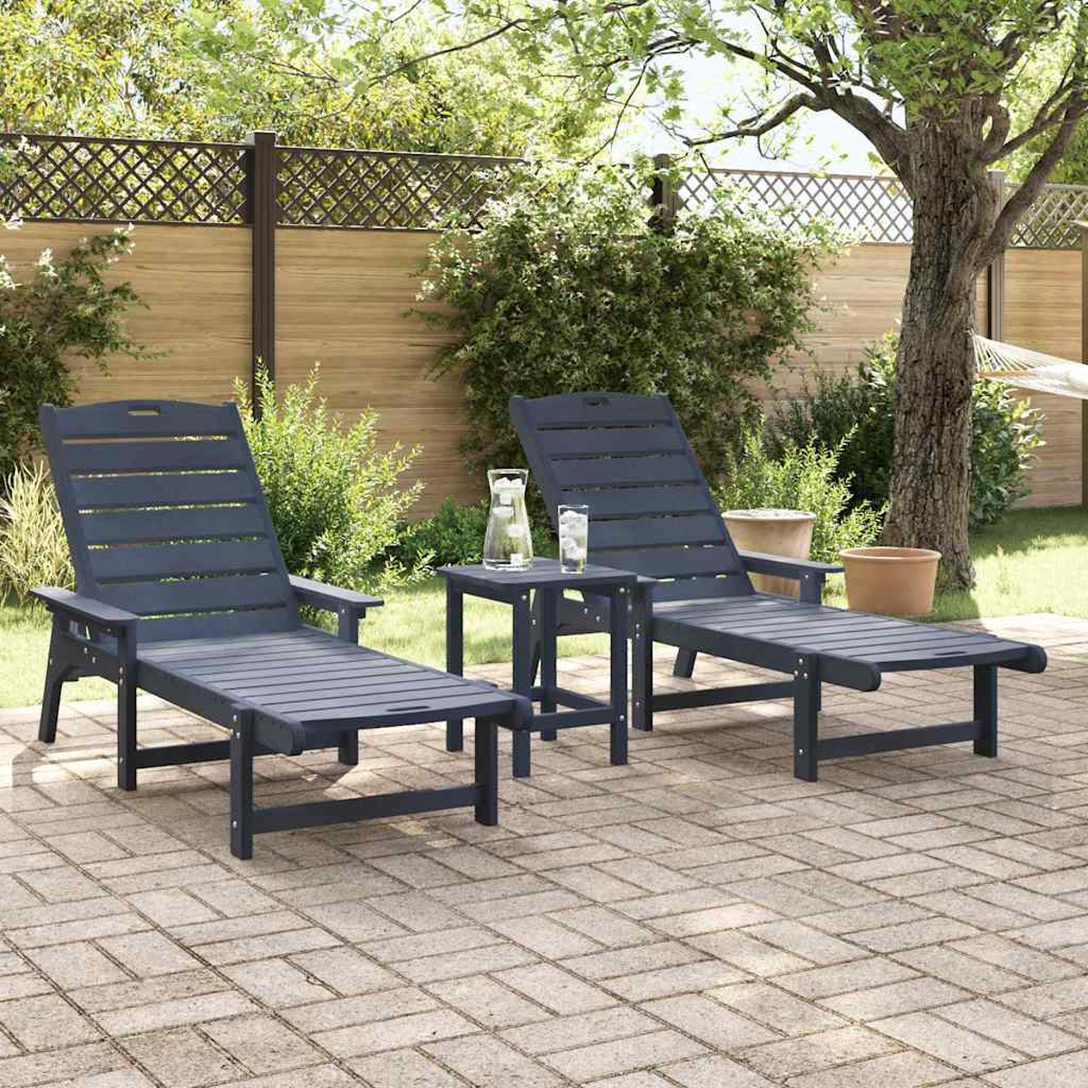 Zwei blaue Liegestühle mit einem kleinen Tisch, einem Krug und zwei Gläsern stehen auf einer Ziegelterrasse. Im Hintergrund sind ein Zaun und Bäume zu sehen.