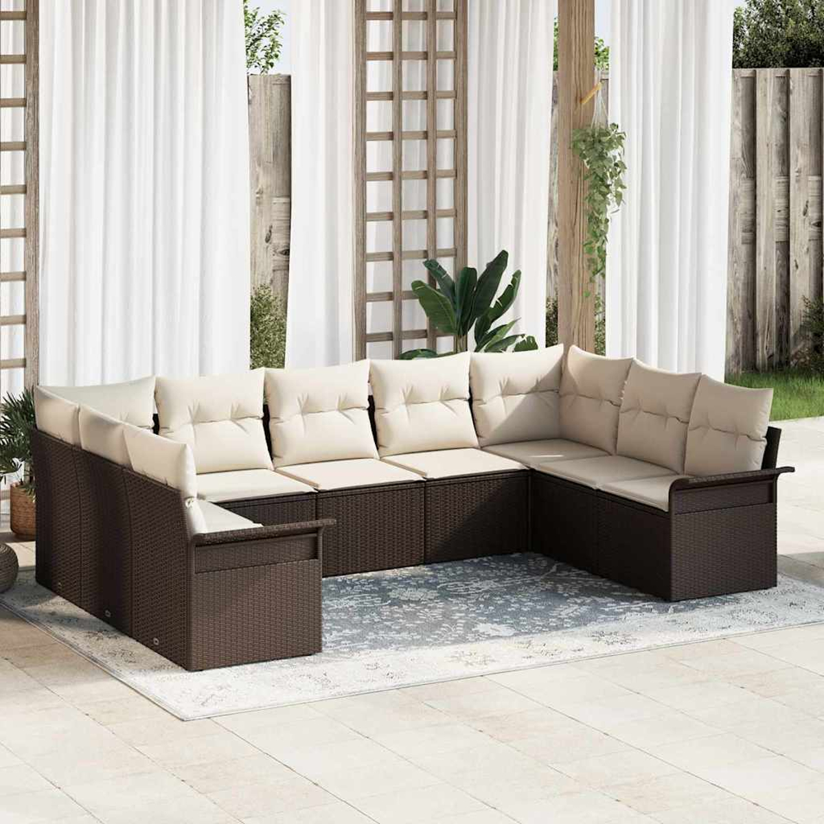 Ein großes, braunes Korbmöbel-Ecksofa mit cremefarbenen Kissen steht auf einem Teppich. Weiße Vorhänge und ein Holzgitter im Hintergrund.