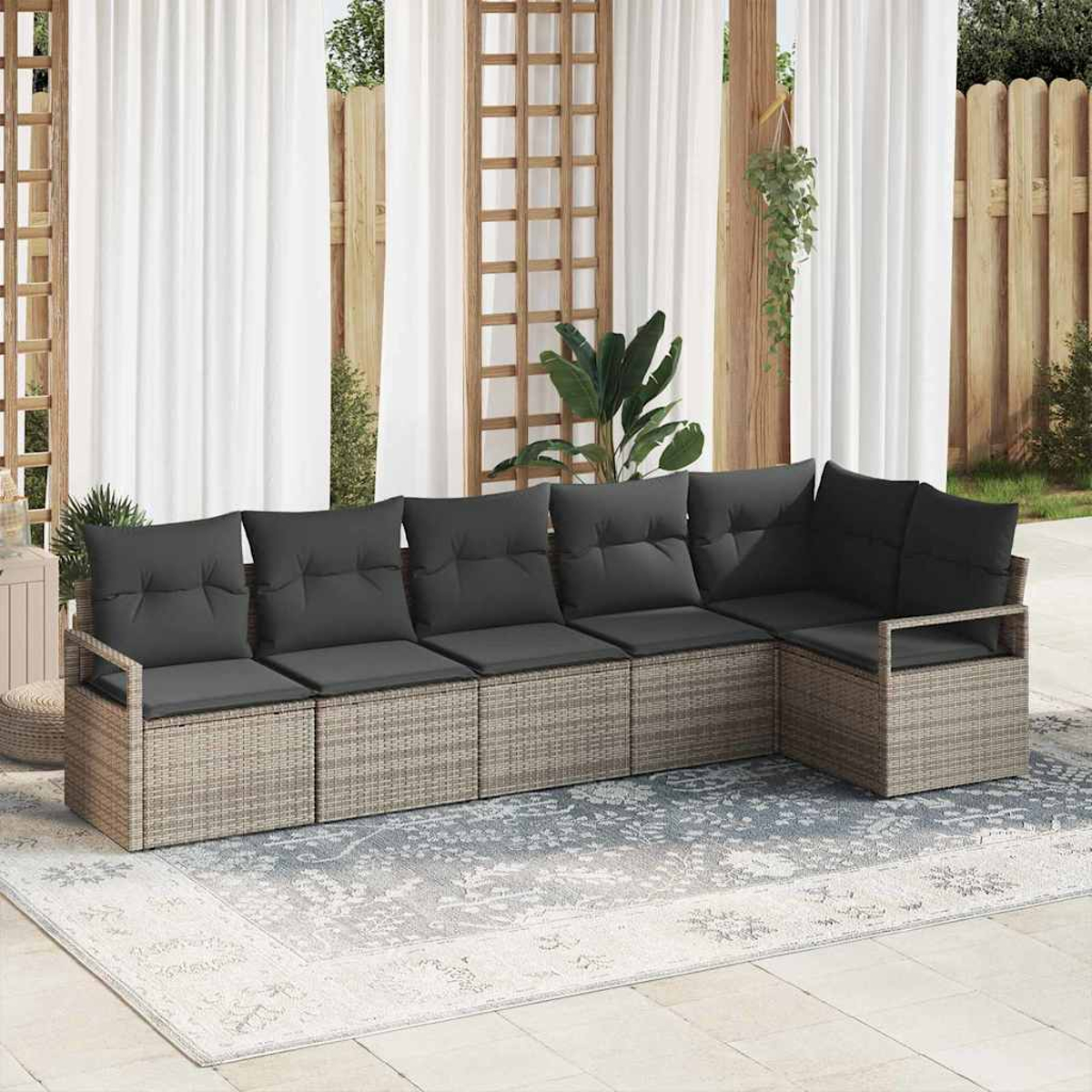 Ein Outdoor-Ecksofa mit grauen Kissen steht auf einem gemusterten Teppich. Weiße Vorhänge und Holzstrukturen sind im Hintergrund.