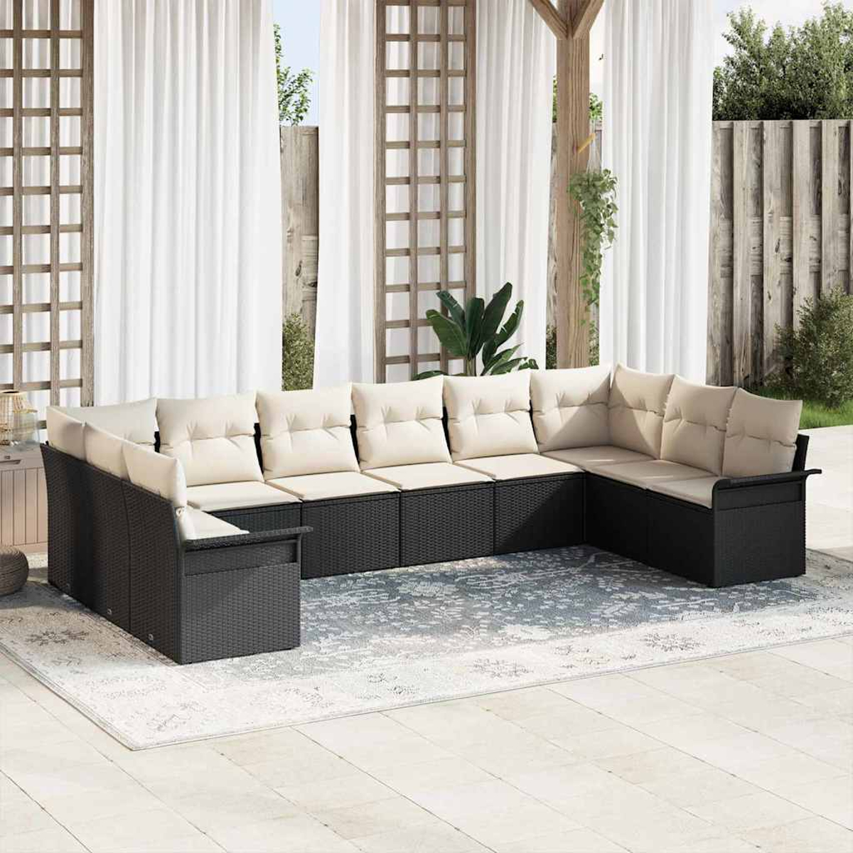 Un sofá negro de mimbre en forma de U con cojines crema está sobre una alfombra. Cortinas blancas y un enrejado de madera en el fondo.