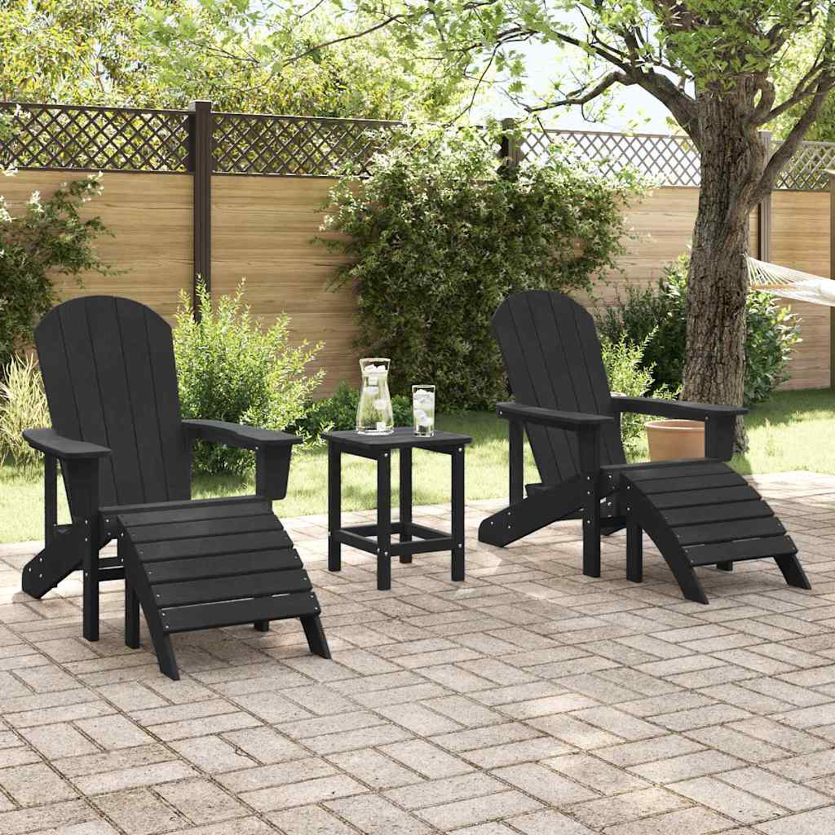 Zwei schwarze Adirondack-Stühle mit Fußstützen und einem kleinen Tisch auf einer Ziegelterrasse. Auf dem Tisch stehen ein Krug und Gläser.
