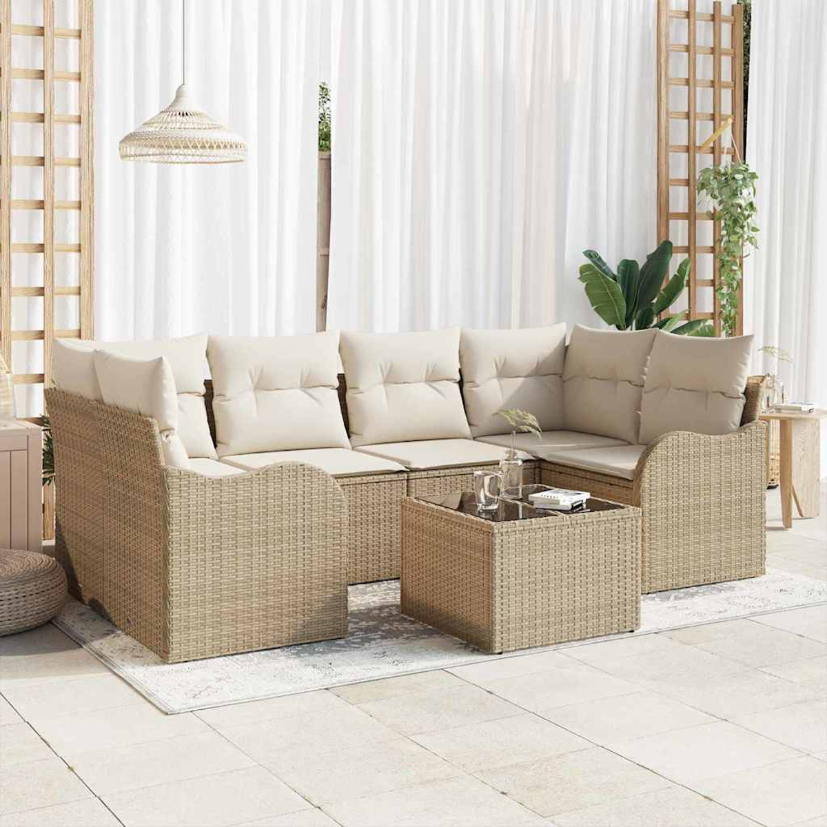 Outdoor-Rattansofa mit cremefarbenen Kissen und Couchtisch. Weiße Vorhänge und Spalier im Hintergrund.