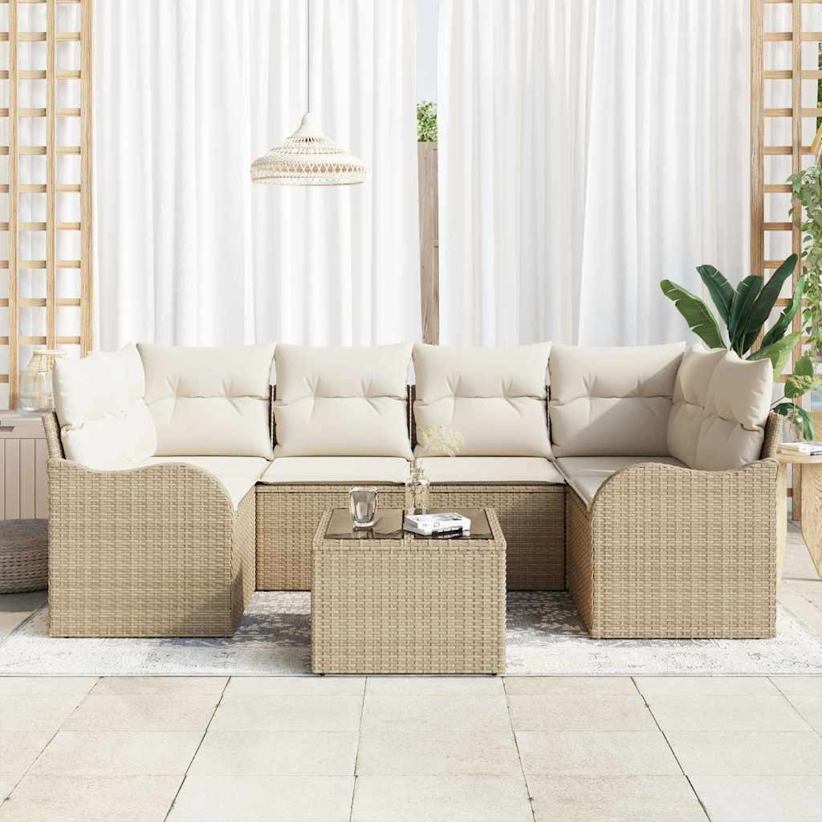 Geflochtenes Sofa mit cremefarbenen Kissen, Glastisch. Weiße Vorhänge im Hintergrund. Dekorative Holzgitter und Pflanzen rechts.
